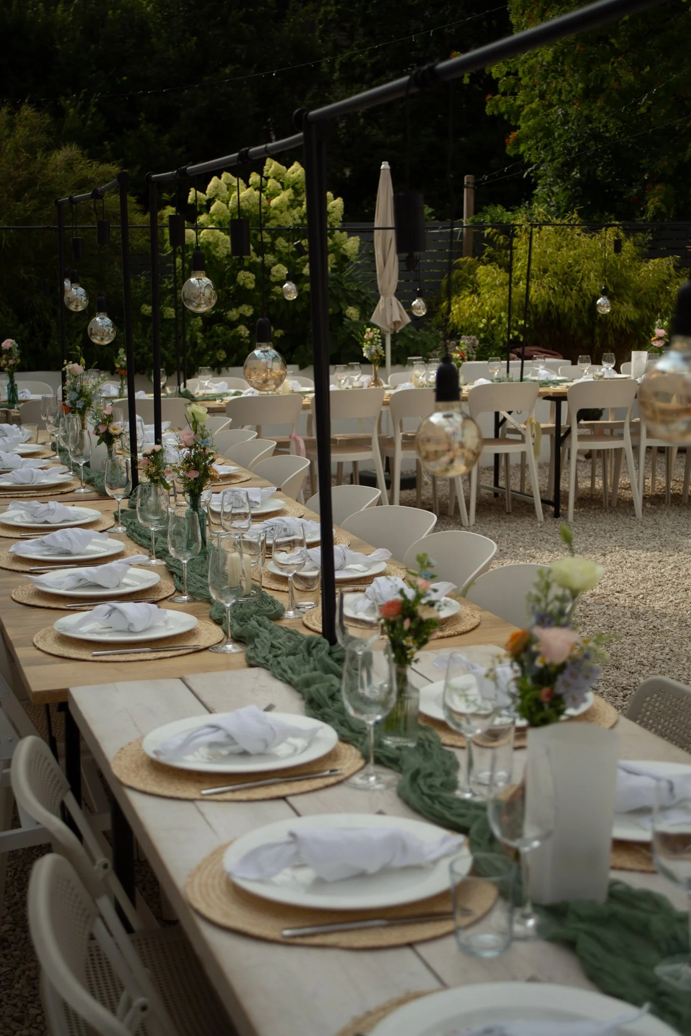Festlich gedeckte Hochzeitstafel im Freien mit Blumenschmuck, Gläsern und Lichterketten.