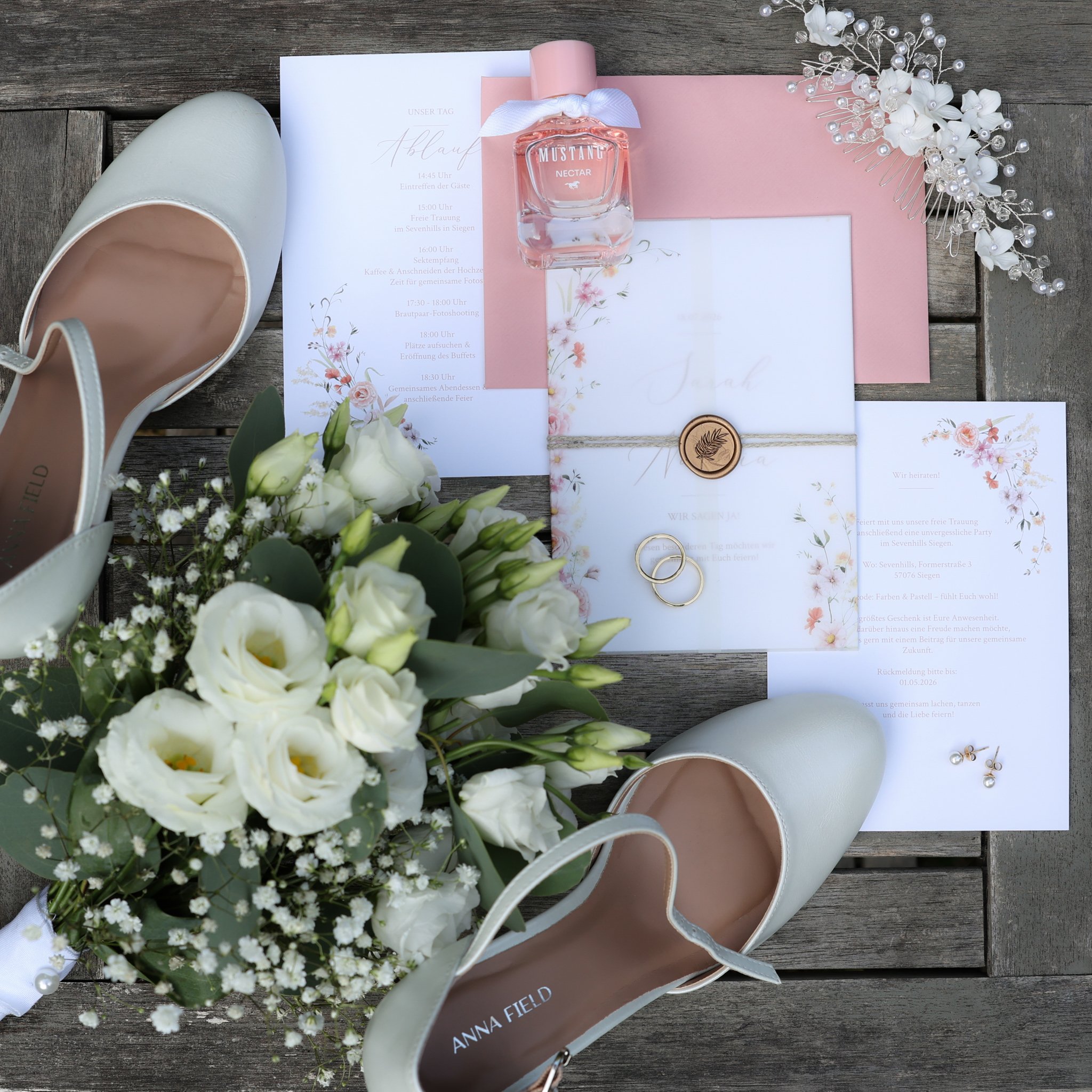 Detailaufnahme einer Hochzeitseinladung mit Parfum, Brautschuhen, Blumen und Brautschmuck.