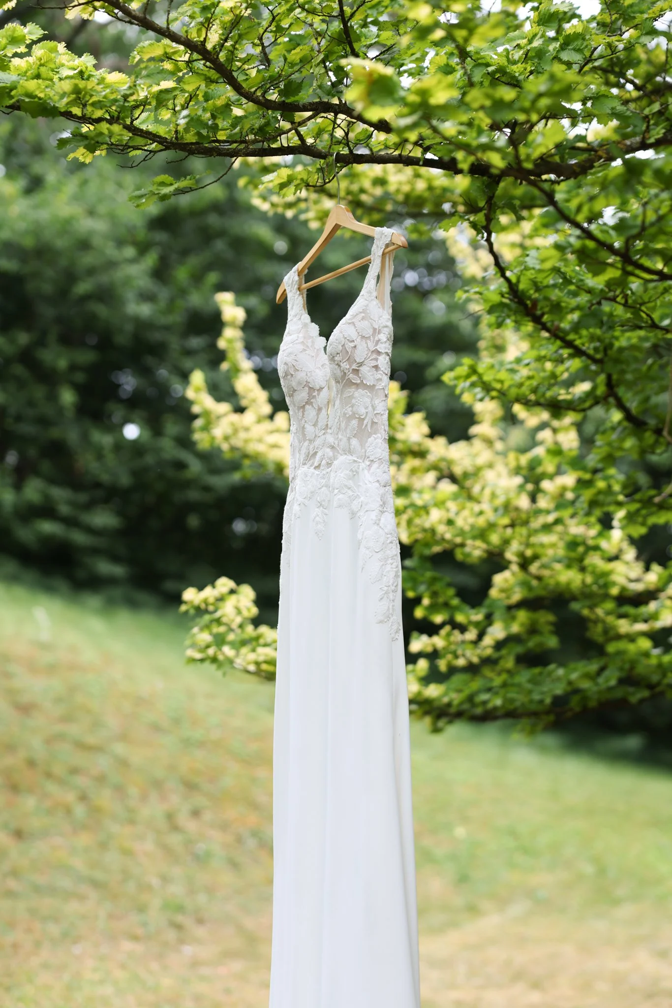 Brautkleid auf einem Holzbügel an einem Baum in einer natürlichen Umgebung aufgehängt.
