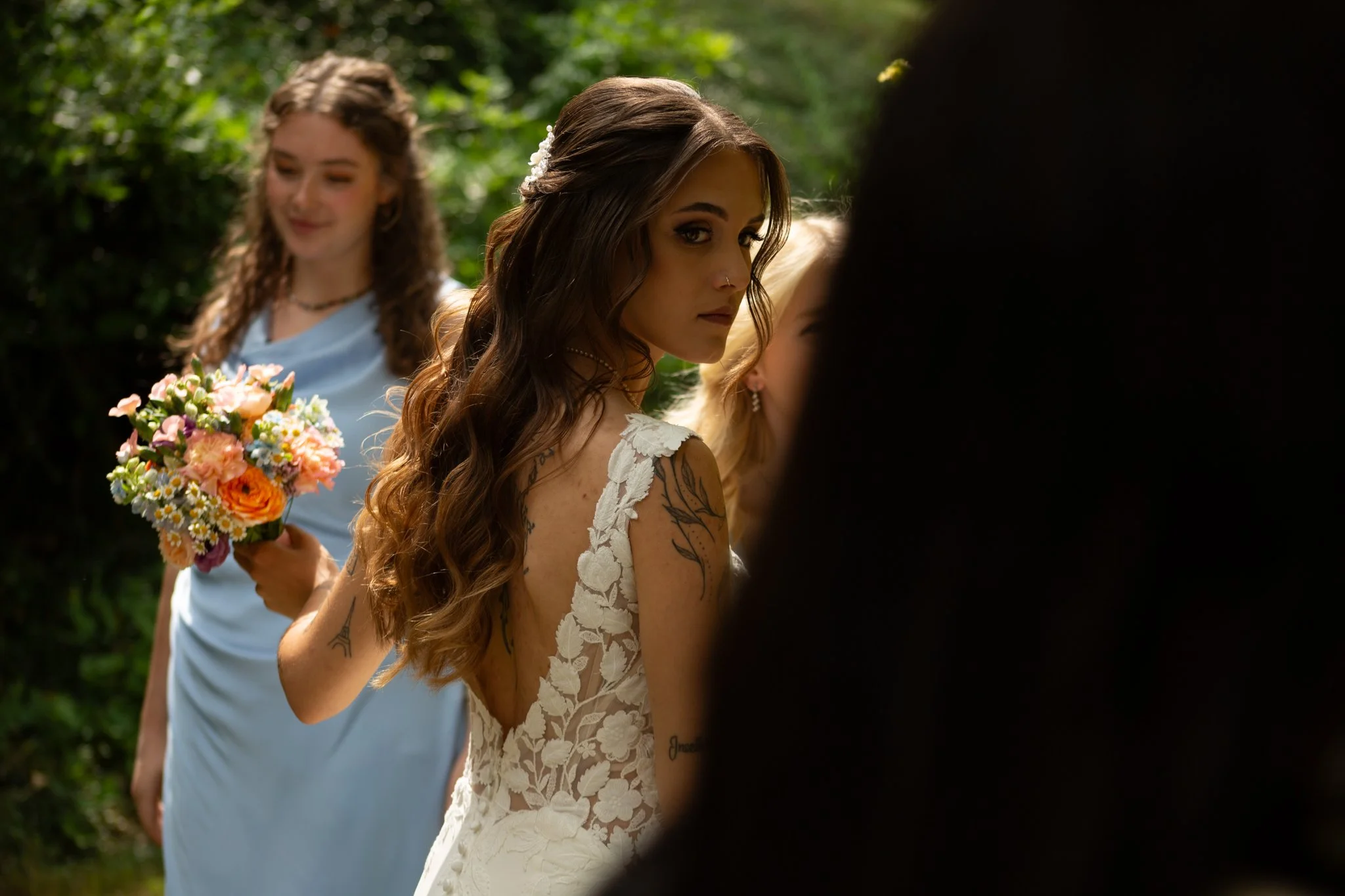 Braut im Spitzenkleid mit floralen Details während der Hochzeitsvorbereitungen im Freien.