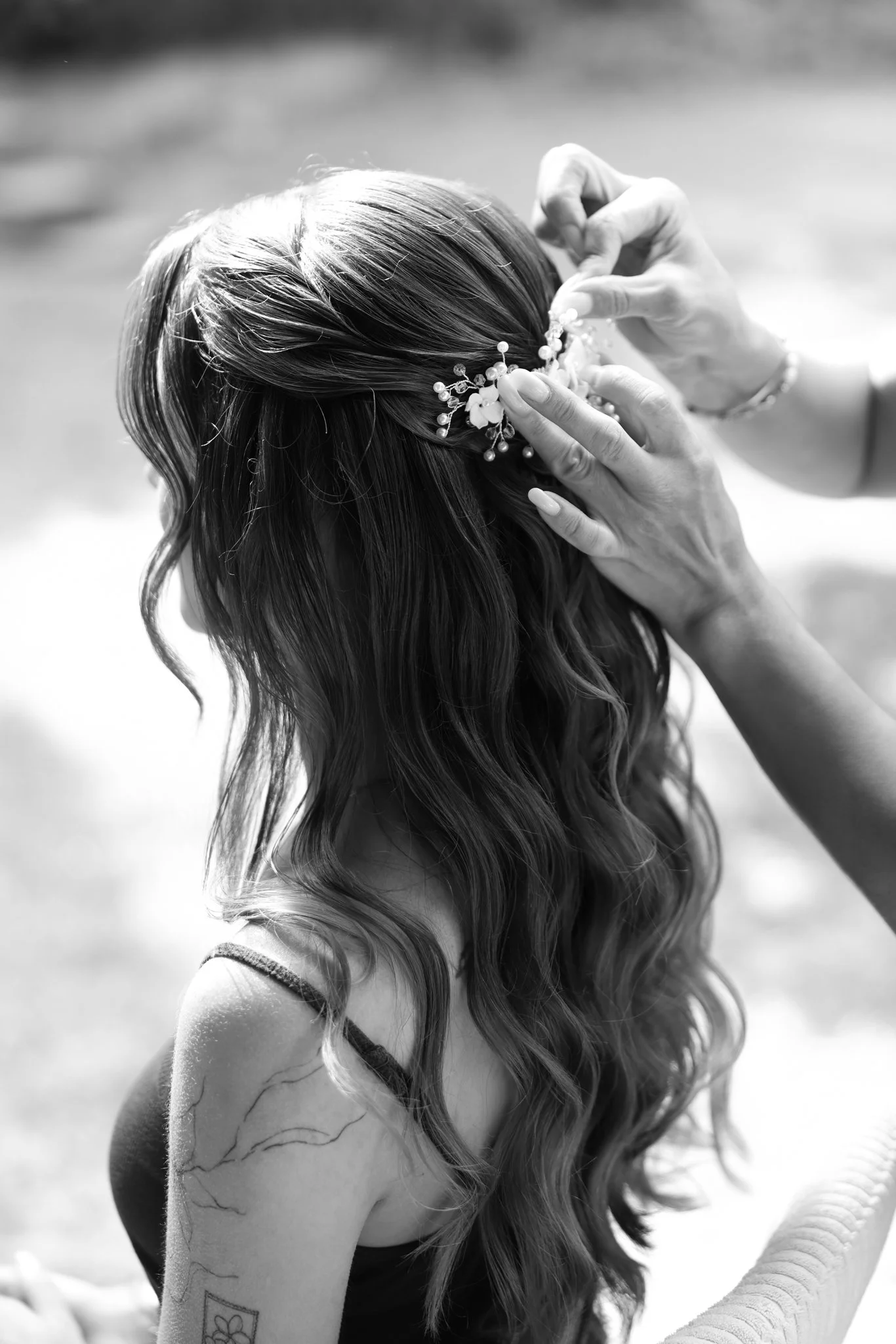 Schwarz-Weiß-Portrait einer Braut beim Einsetzen ihres Haarschmucks während des Stylings.