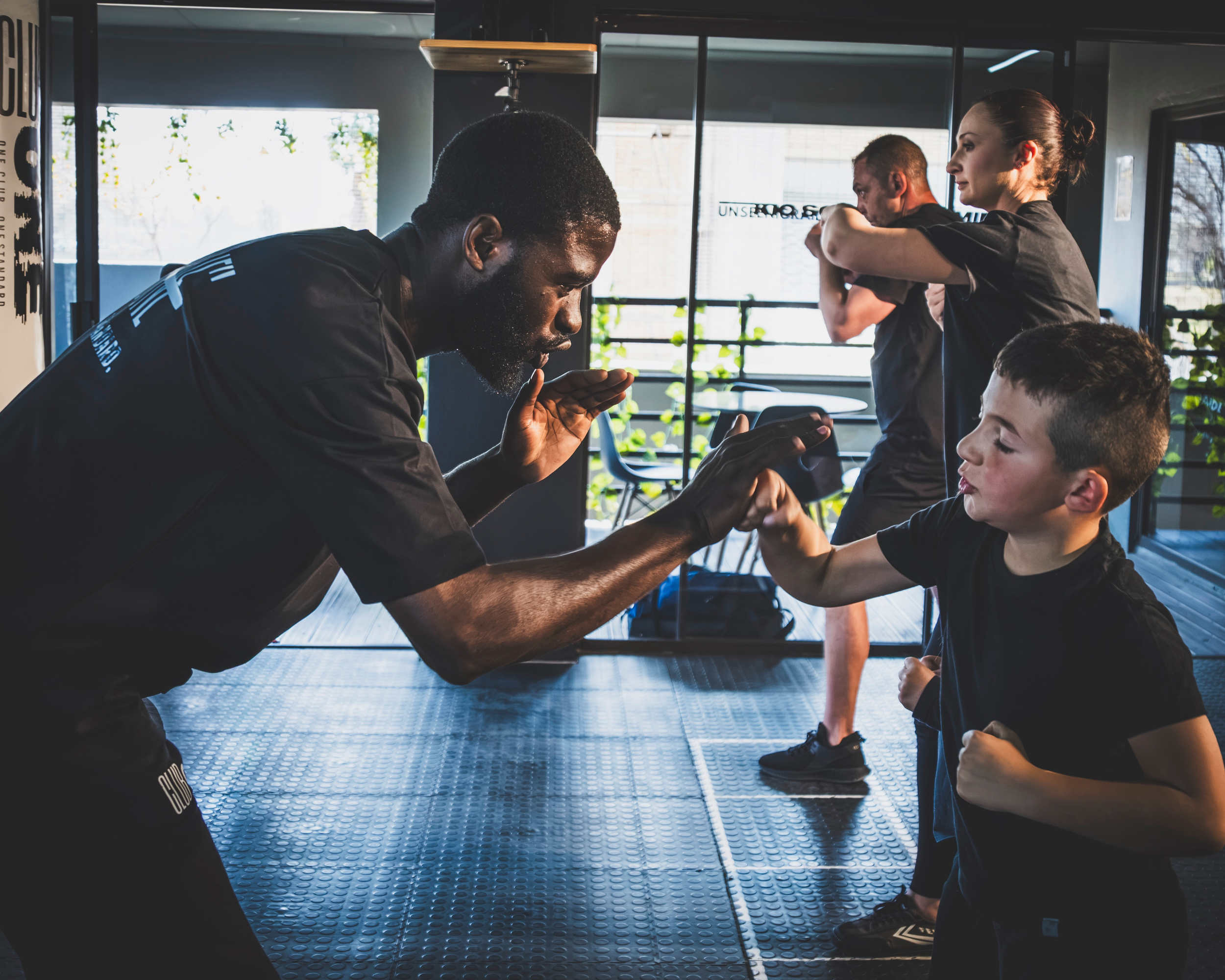 A trainer and young boy in a gym engaged in arm wrestling during a fitness class or training session.