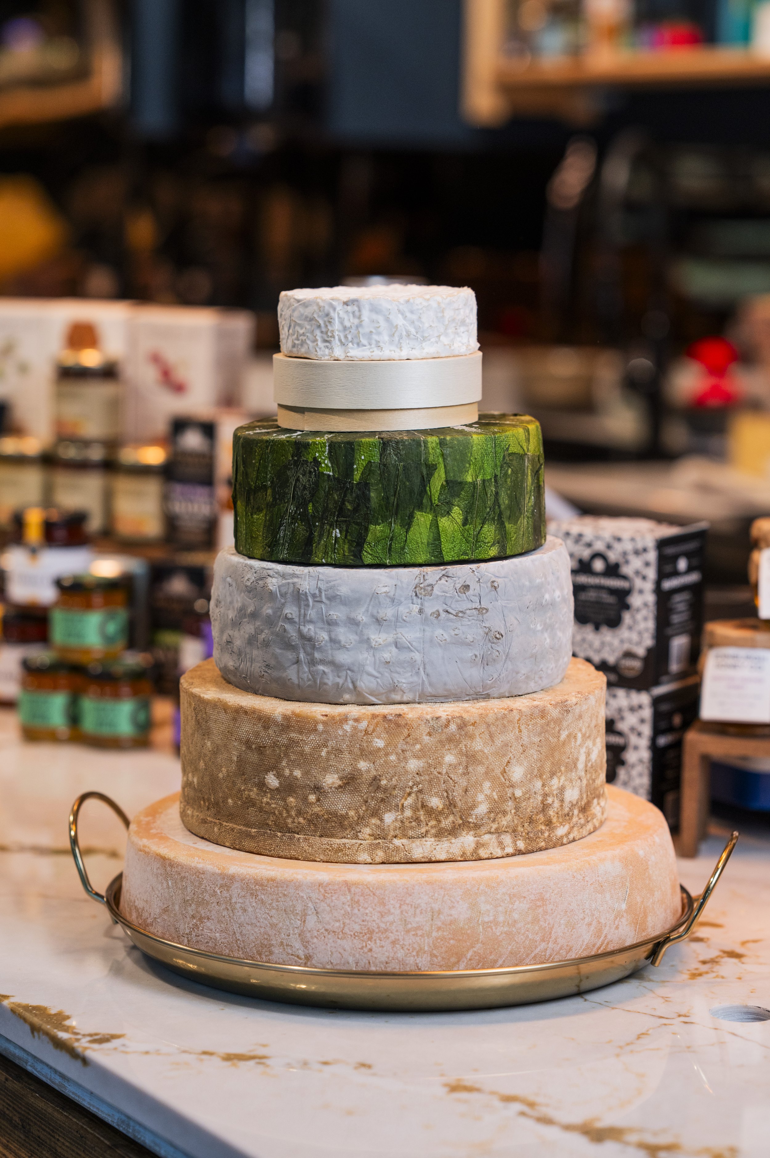 Stacked wheels of artisanal cheese on a marble cheese board in a shop or market.