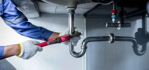 A plumber working under a sink, using a wrench to tighten a pipe fitting