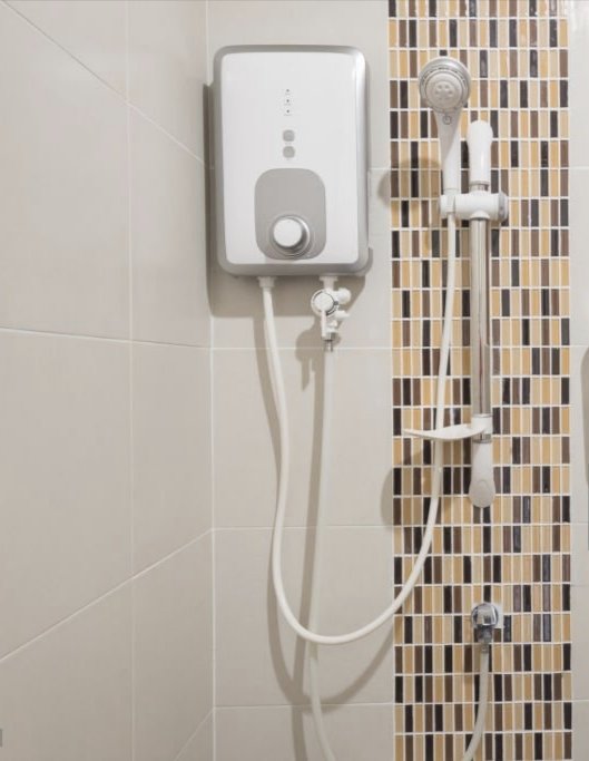 Electric water heater mounted on a tiled bathroom wall with a connected showerhead and hose.