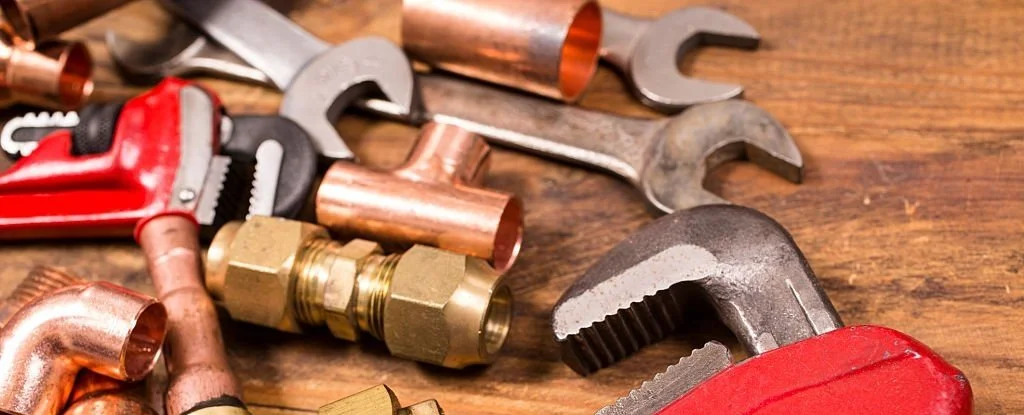 Assorted plumbing tools and copper pipes on a wooden surface.