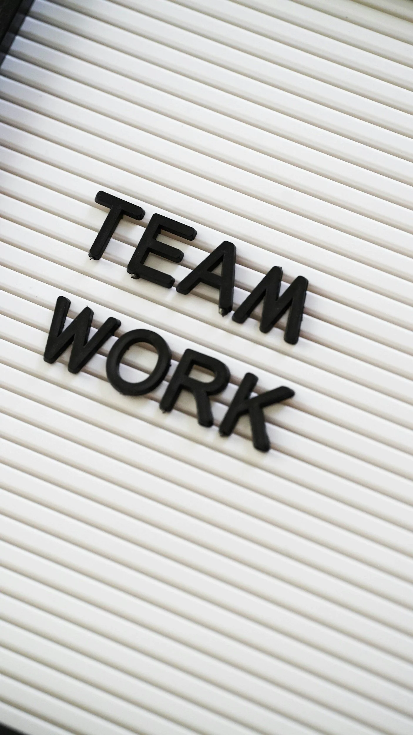 A letter board displaying the words 'TEAM WORK' in black plastic letters on a white background with horizontal ridges.