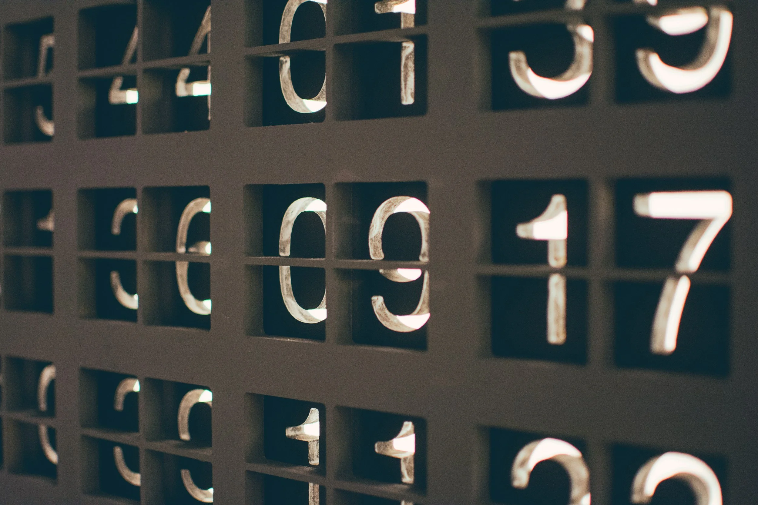 Close-up of a black grid with numbers cut out, with light shining through the cutout sections