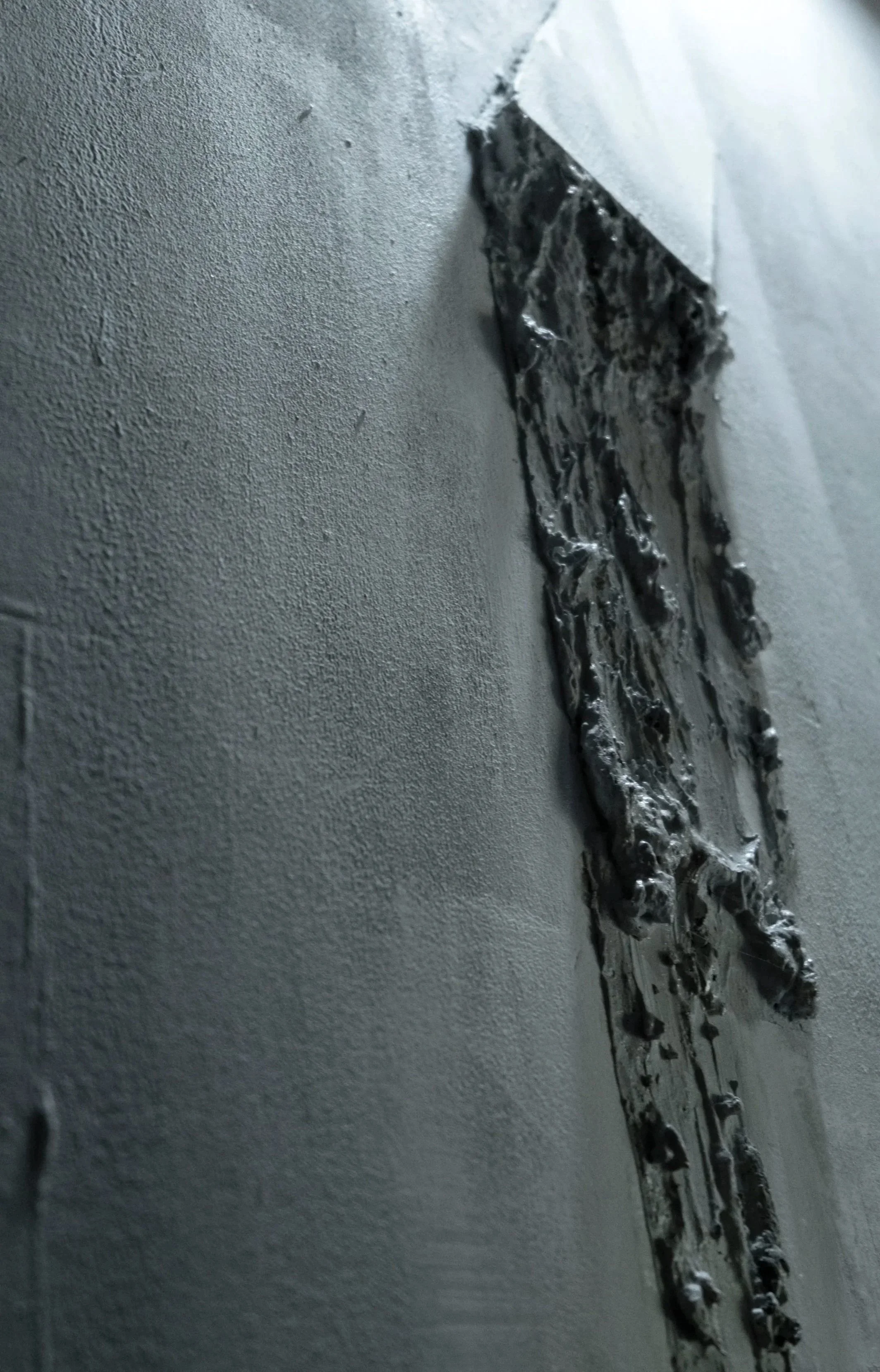 A close-up of a piece of black tape or foil adhered to a textured, smooth white wall.