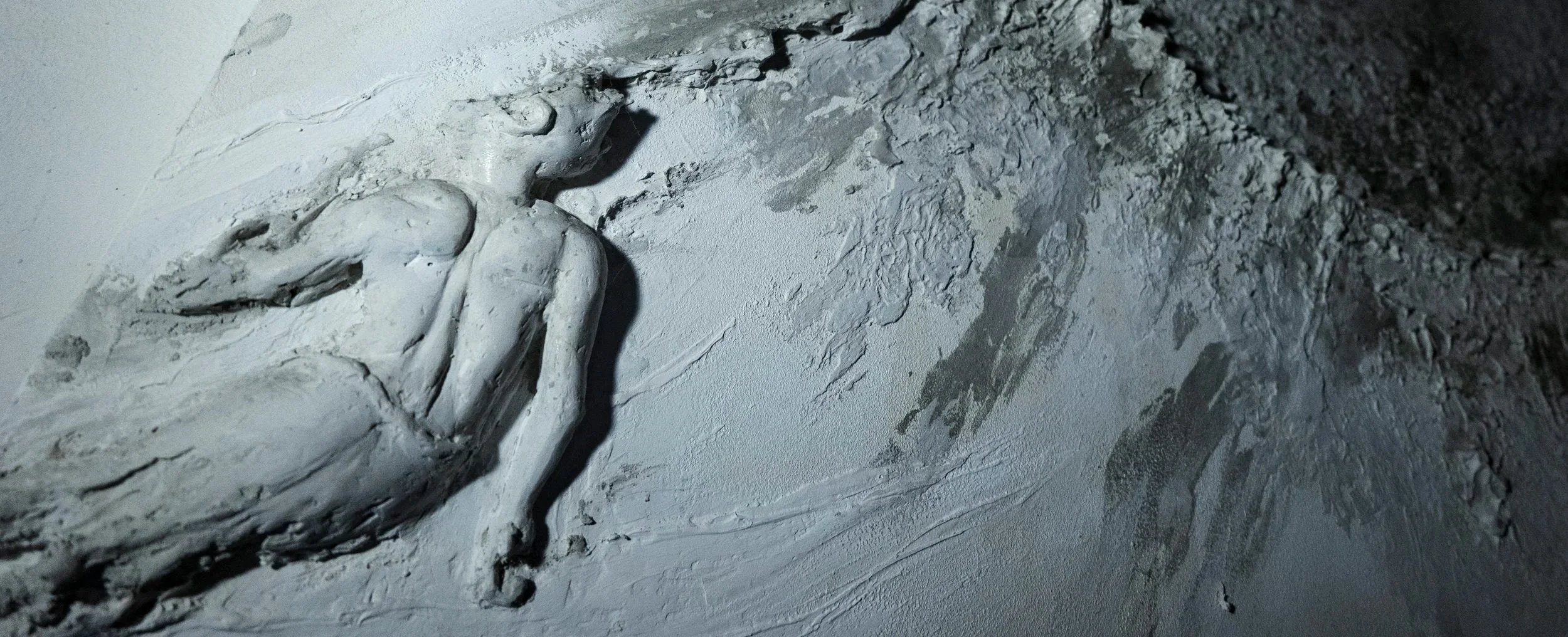Statua di una figura umana distesa in plastilina bianca che si disgrega , su un universo di pietra lavica e cemento