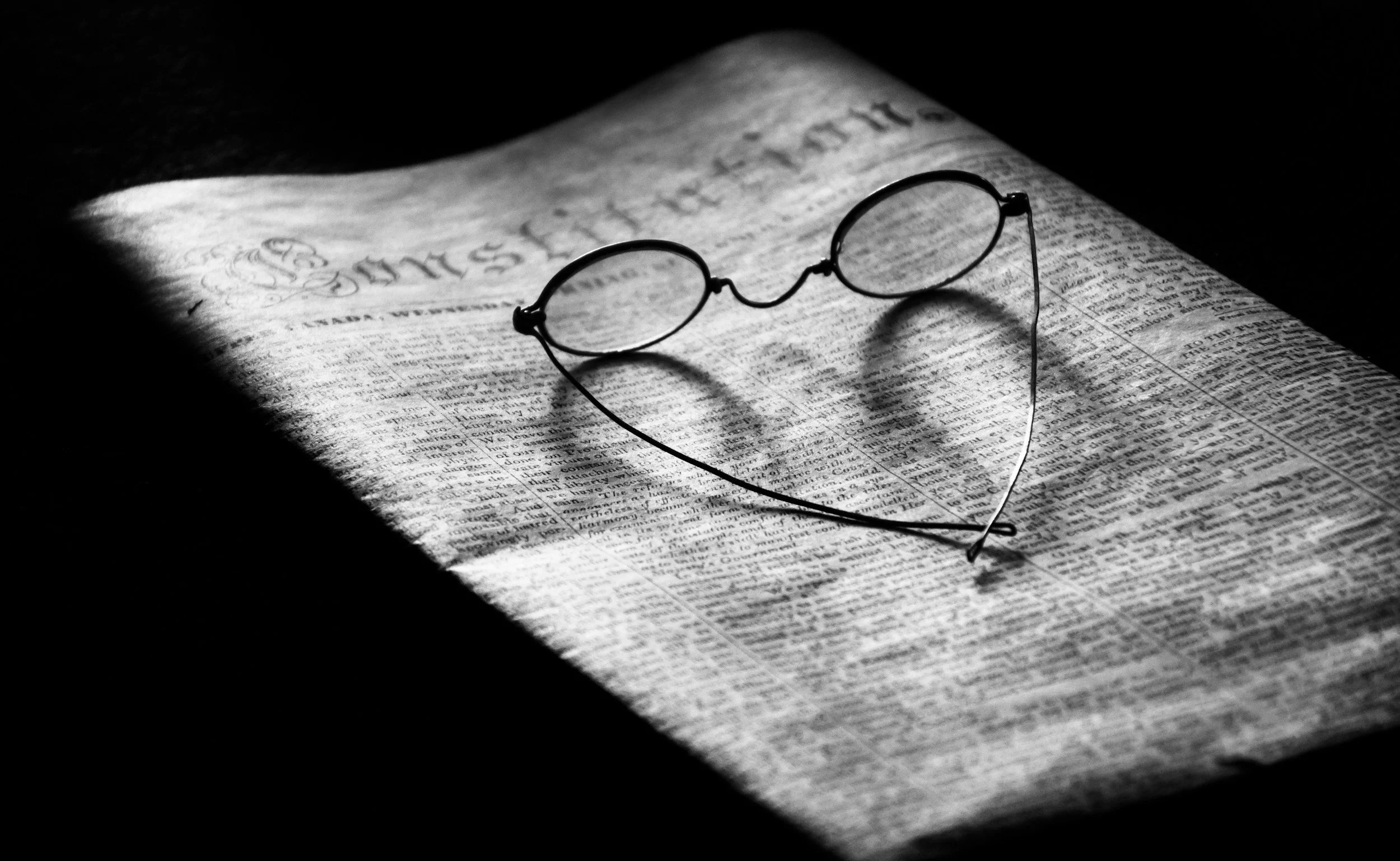 Black and white photo of reading glasses resting on an open newspaper.