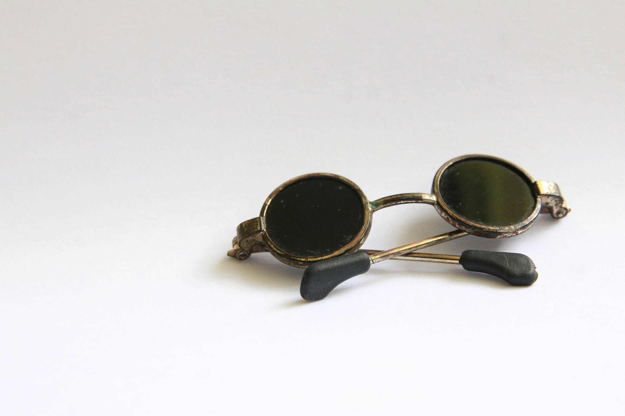 Pair of vintage sunglasses with round black lenses and metal frame lying on a white surface.