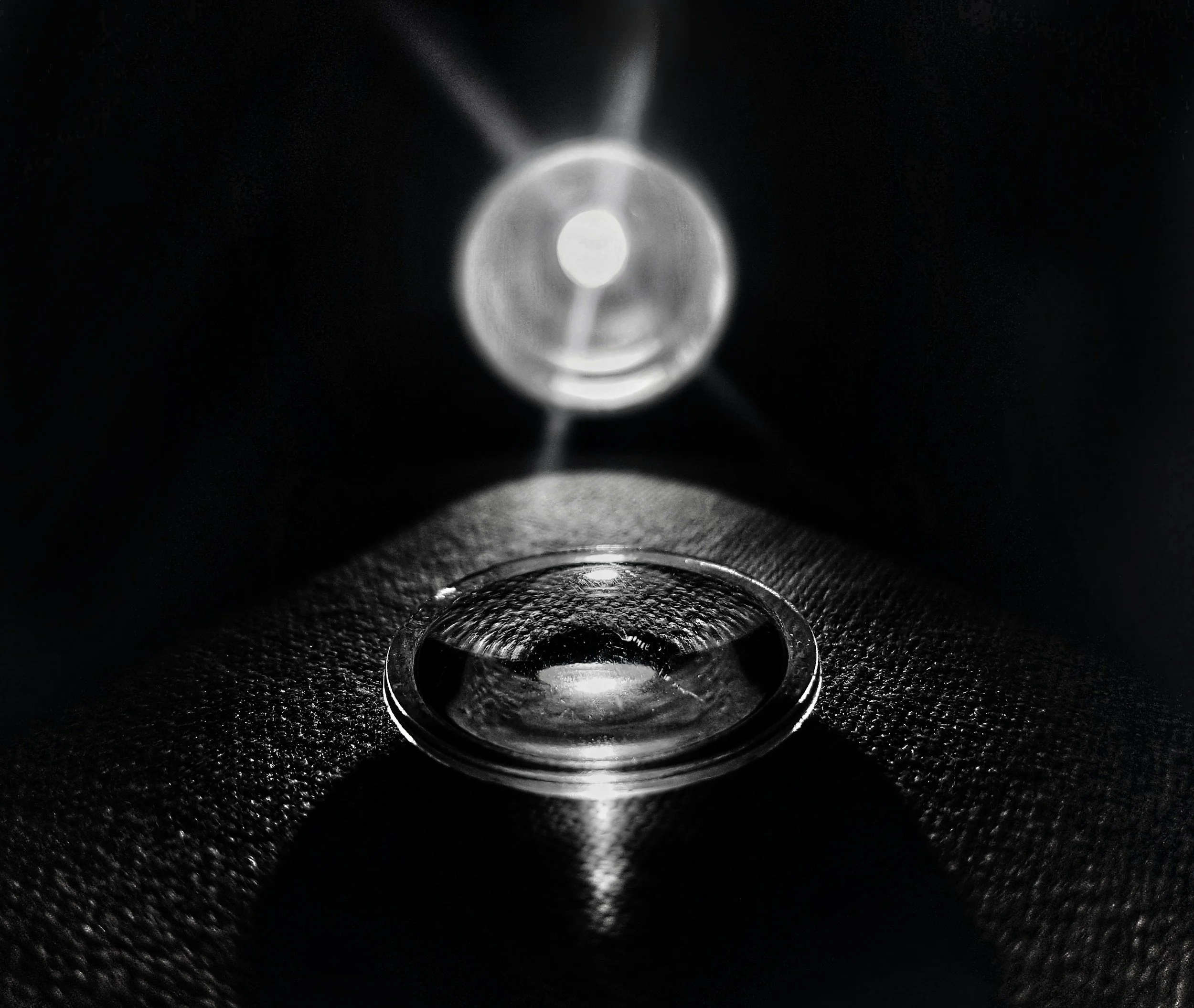 Close-up of a metallic, hollow object with a circular opening, reflecting light and creating shadows on a textured dark surface.