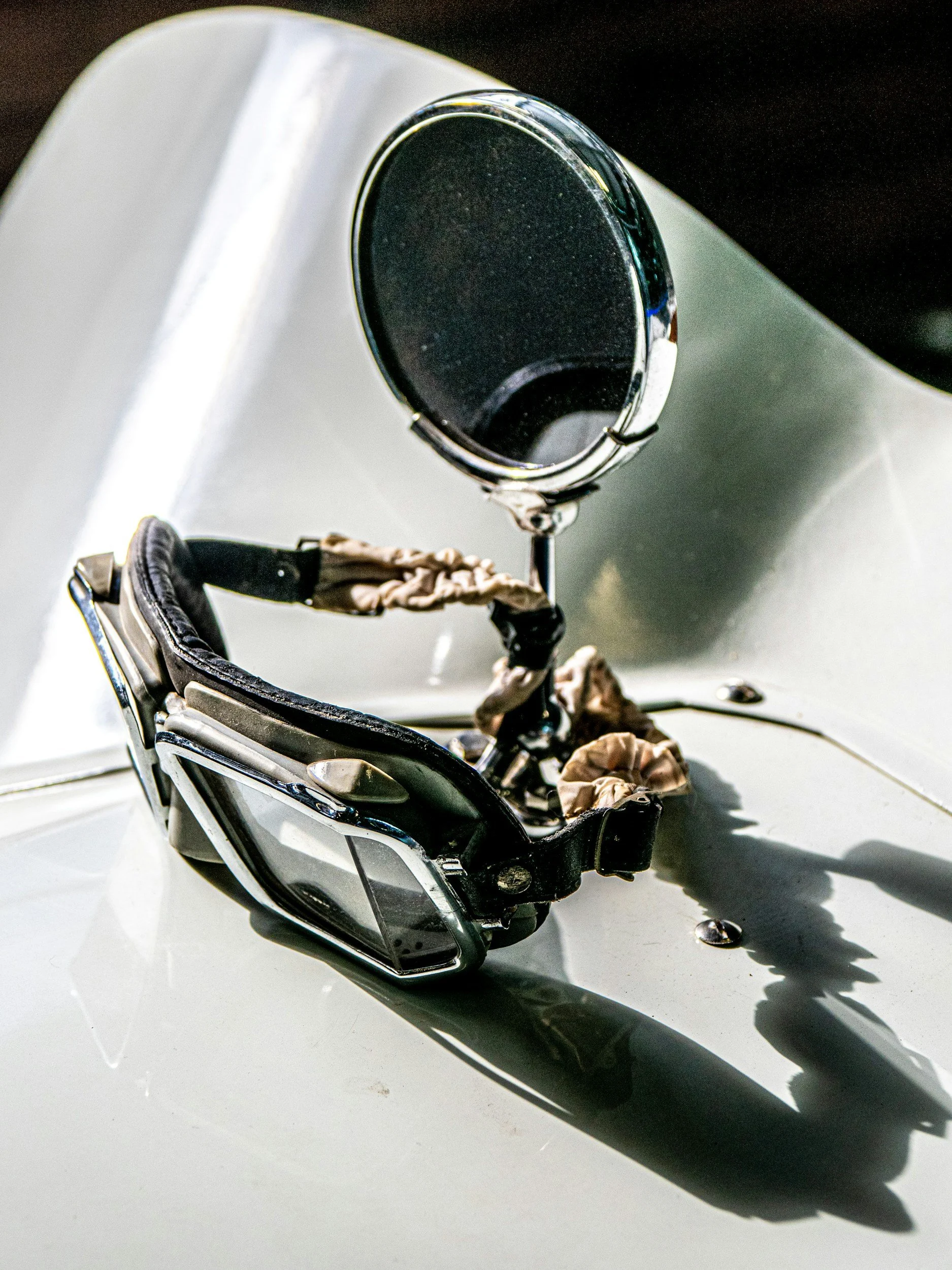 A pair of sunglasses with black lenses and a metallic frame resting on a white surface. The sunglasses cast a shadow and some small objects are nearby.