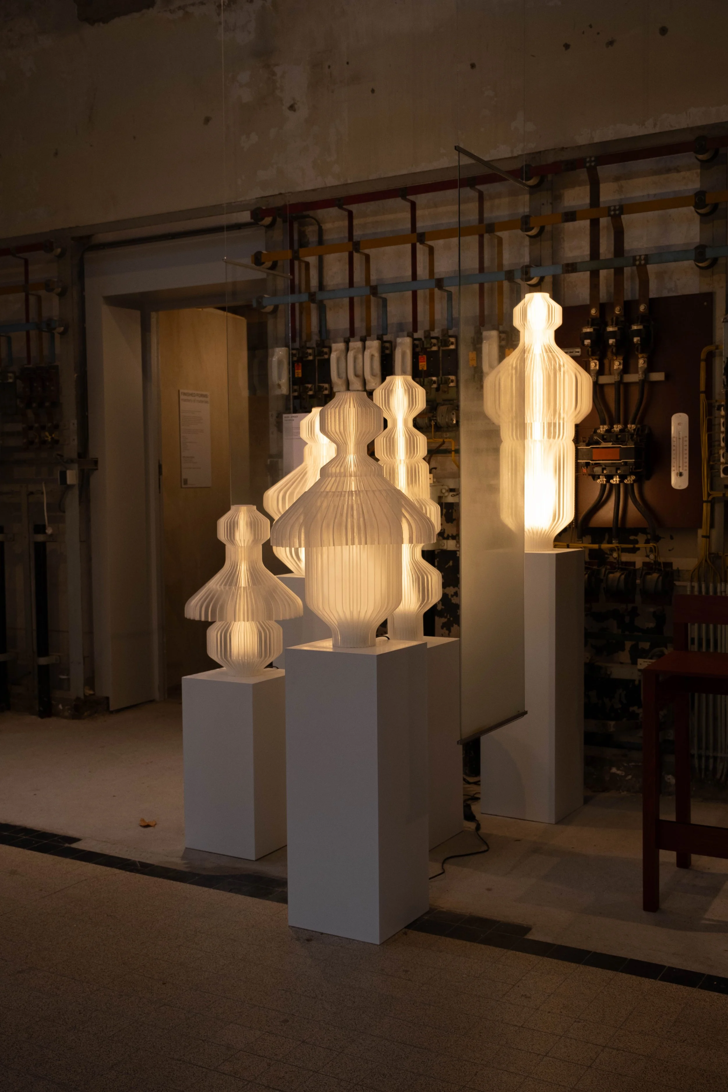 Modern pendant lights on display, illuminated, with a background of electrical boxes and pipes on an industrial-style wall.