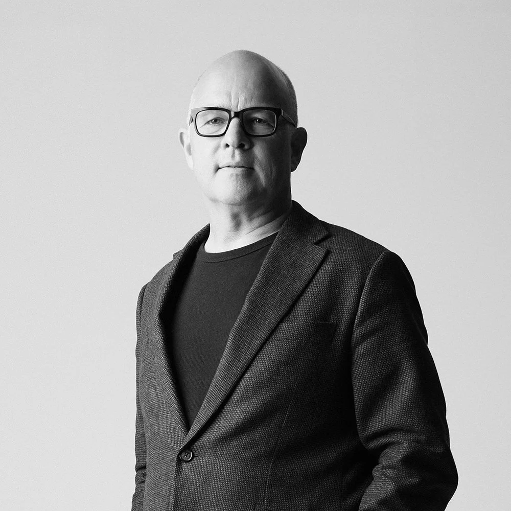 Black and white portrait of Stephen Waddington wearing glasses, a blazer, and a black t-shirt, standing against a plain background.