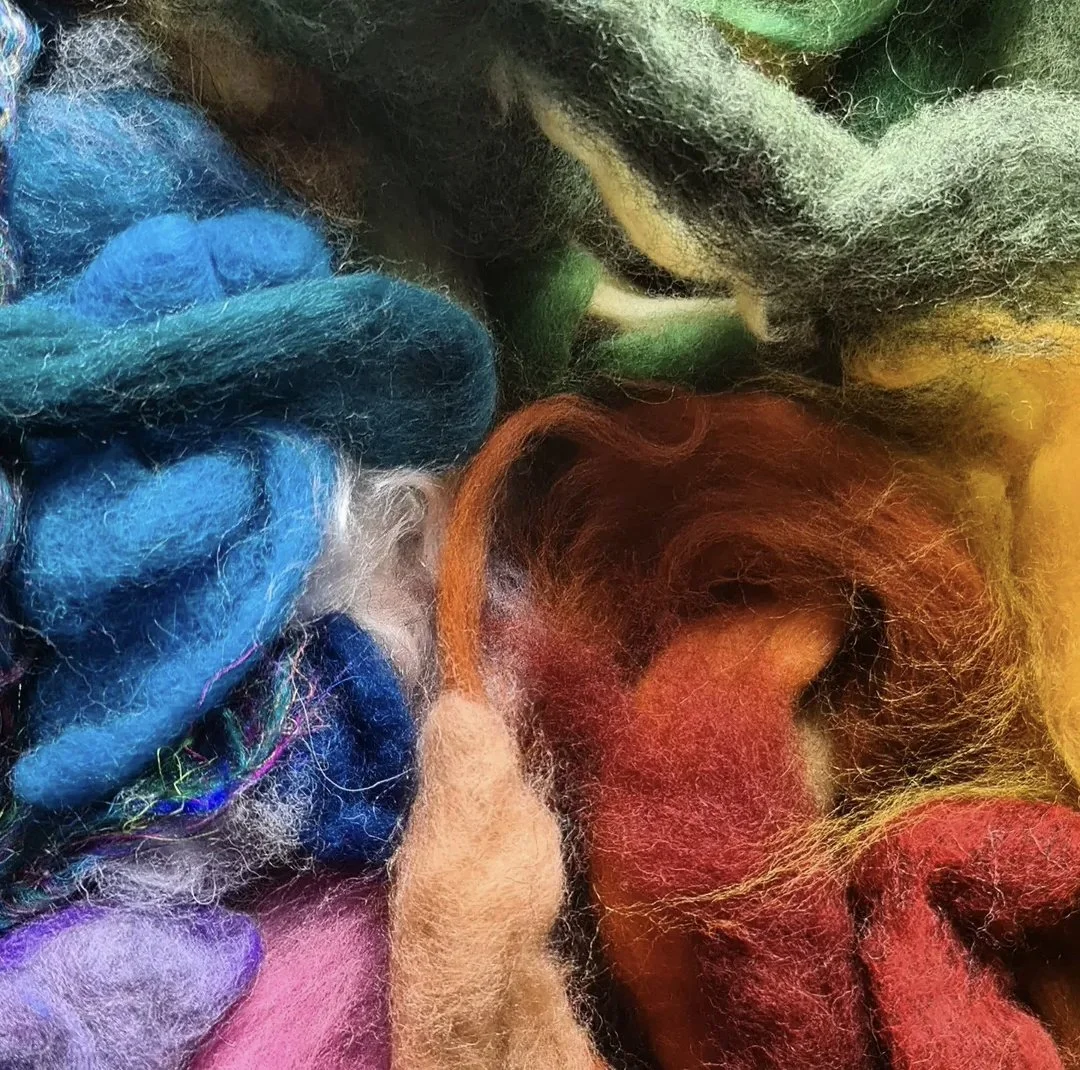 Close-up of colorful felted wool fibers in various shades including blue, green, yellow, orange, red, purple, and white.