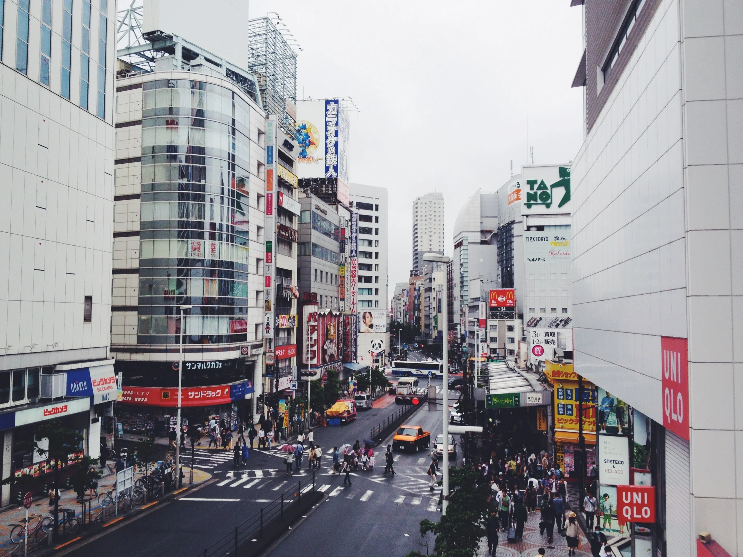 City street scene with tall buildings, many store signs, and pedestrians crossing the street.