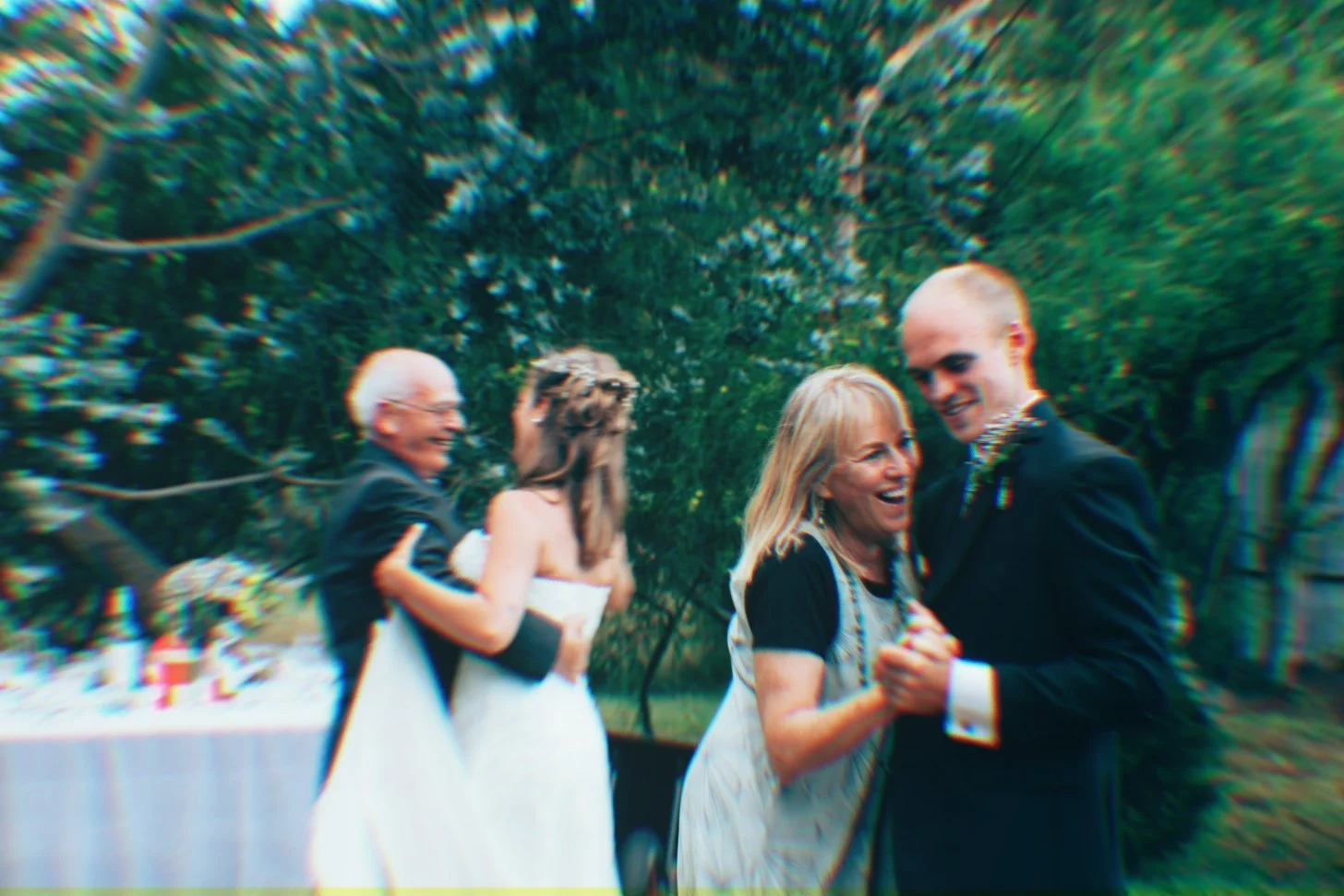 People dancing and celebrating outdoors at a wedding reception with lush green trees in the background.
