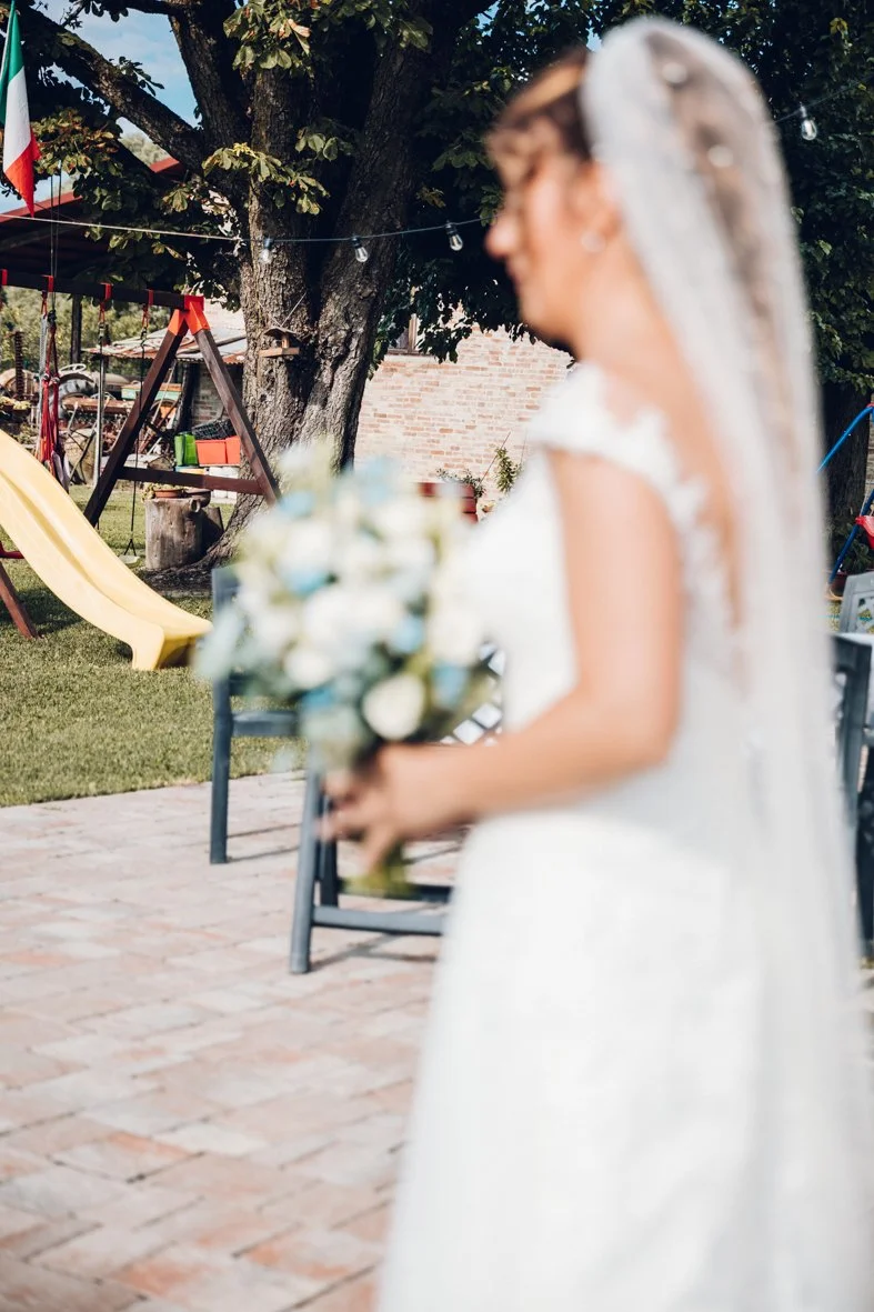 Blurred bride in a white wedding dress holding a bouquet outdoors with trees, a slide, and patio furniture in the background.