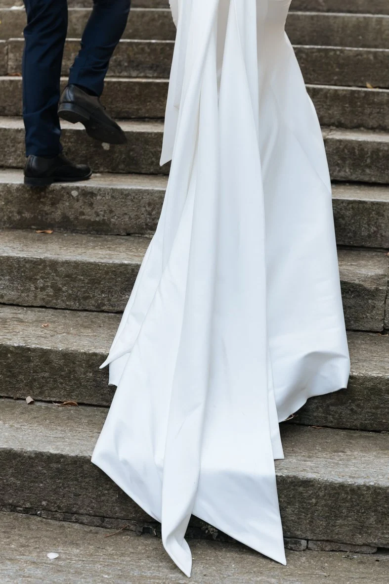 Bride and groom walking up outdoor stone steps, bride wearing a long white gown, groom in black shoes and dark pants.