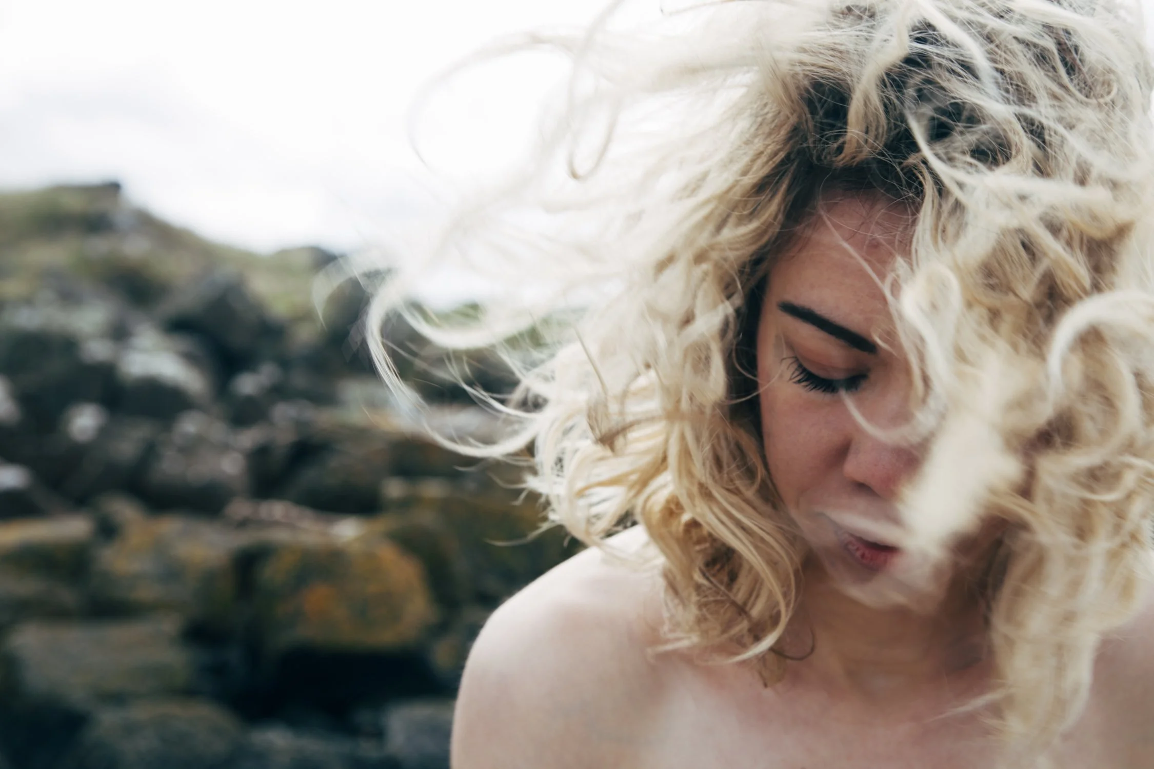 Donna con capelli ricci biondi, occhi chiusi, capelli mossi e atmosfera naturale sul mare o sulla spiaggia.