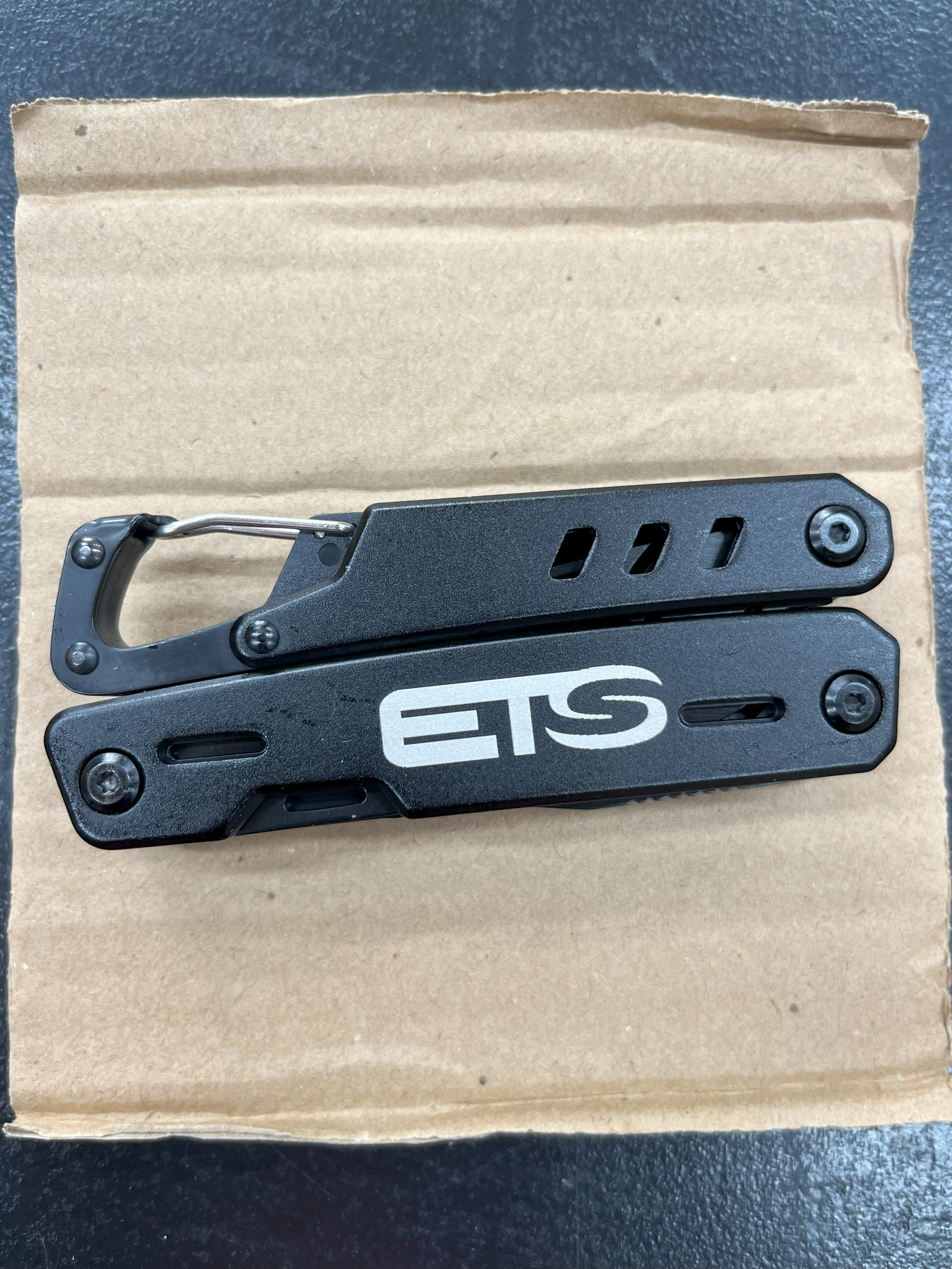 Ein schwarzes Taschenmesser mit Klipp und Riegel, das auf einem braunen Karton liegt.