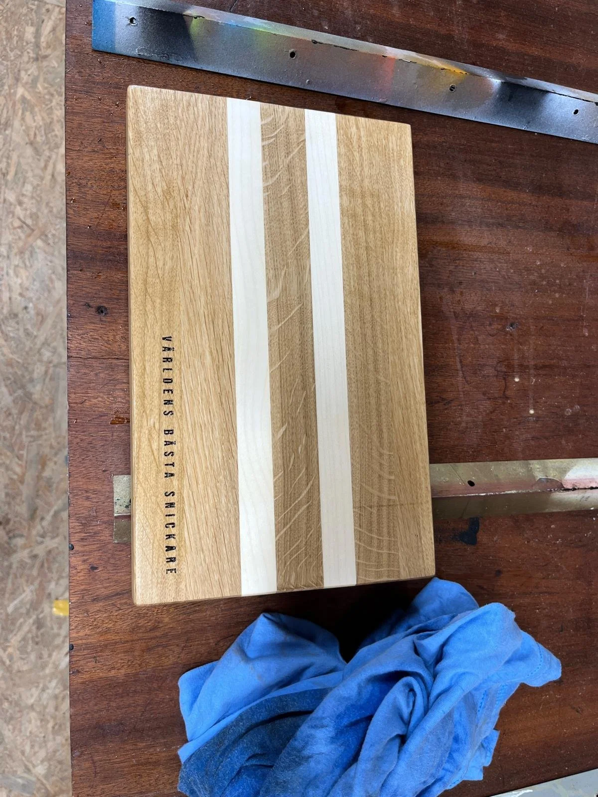 Ein Holzbrett mit zwei weißen Streifen, auf einem Tisch. Das Brett hat aufgedruckten Text, der 'VARIERS BASTA SNICKARE' lautet.