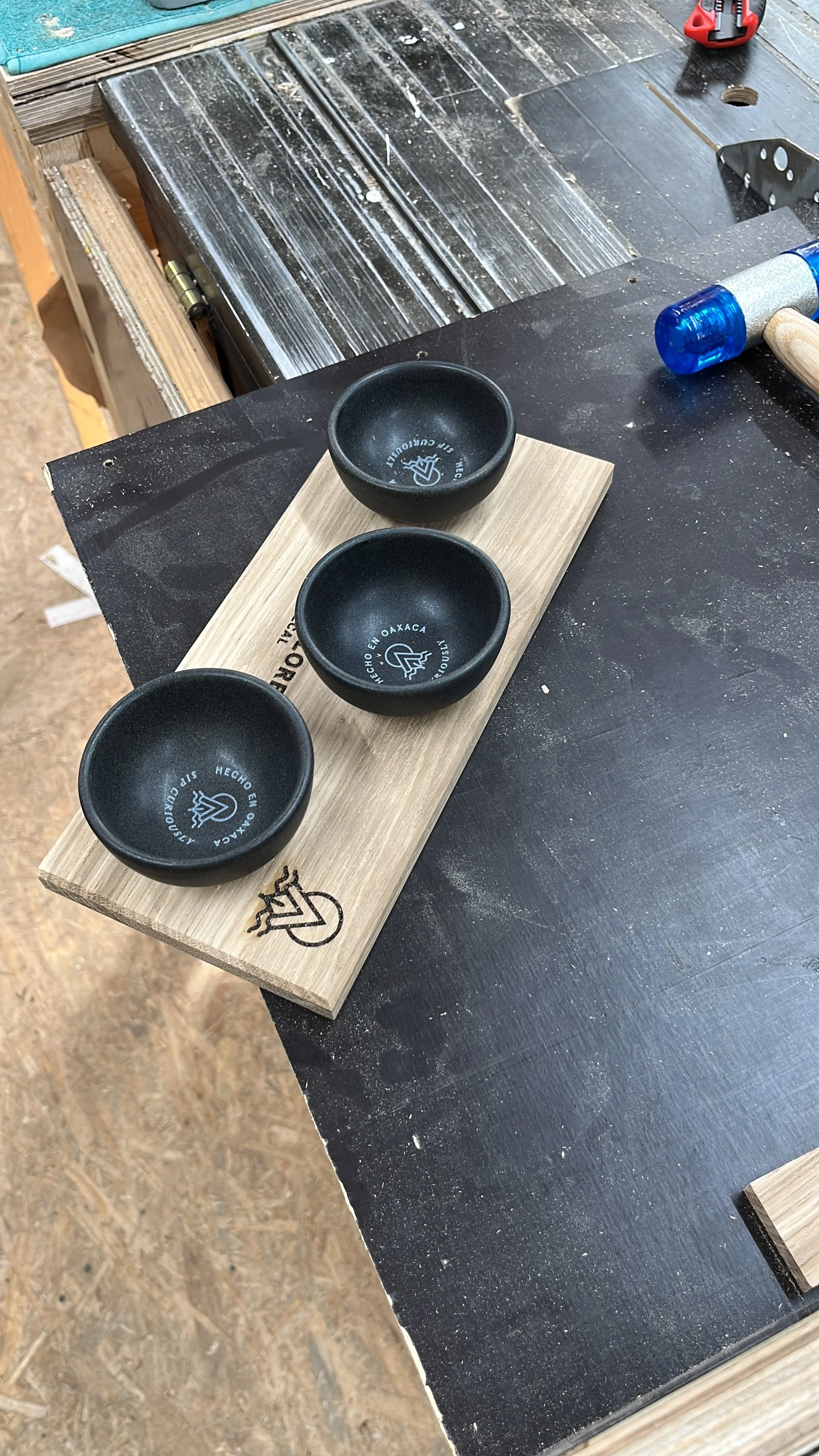 Drei schwarze Keramikschalen auf einem Holzbrett, auf einem schwarzen Arbeitstisch in einer Werkstatt.