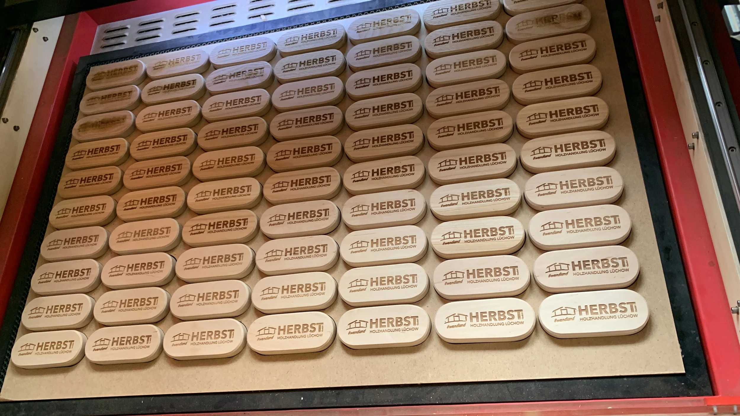 Holzmodelle mit dem Aufdruck 'HERBST', auch mit der Beschreibung 'Holzhandlung Löchow' und einem Haus-Logo, liegen in einer roten und schwarzen Verpackung.