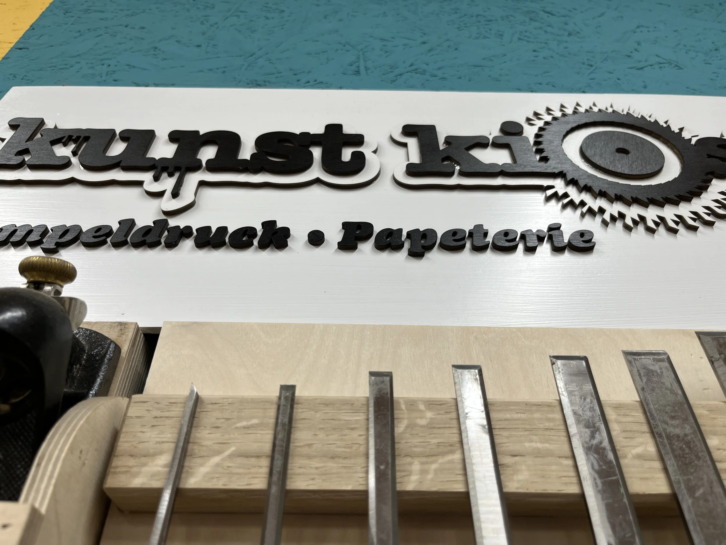 Ein Werkstück mit den Marken "Kunst", "Mauer" und "Papier" auf einer Werkbank, die von einer Maschine beim Schneiden oder Fräsen bearbeitet wird.
