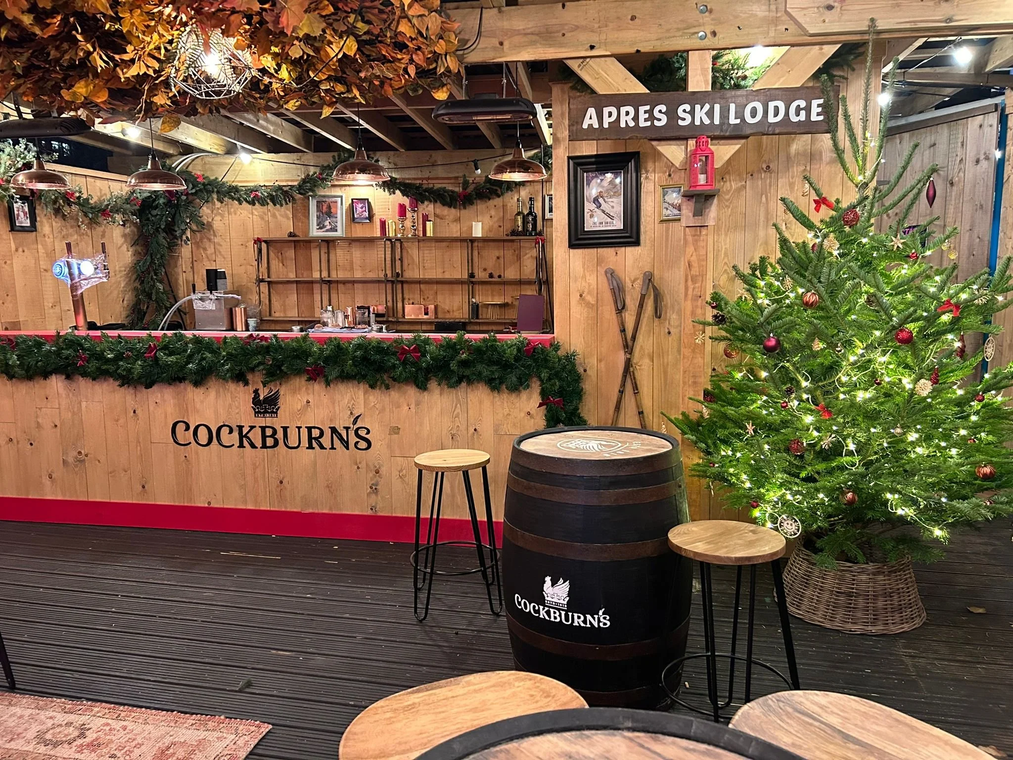 Gemütliche Skihütte mit Holzdekoration, Weihnachtsbaum mit Lichtern und Ornamenten, Barbereich mit Getränken, Skiwachsen an der Wand. Festliche Weihnachtsdekoration mit Tannenzweigen und roten Schleifen.
