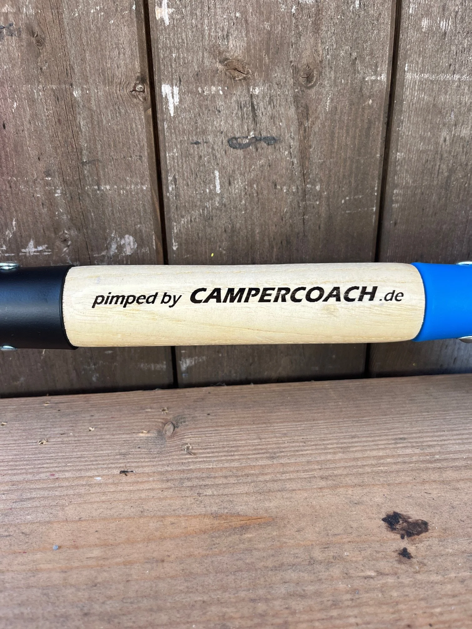 Holzlatte mit der Aufschrift 'pimped by CAMPERCOACH.de' auf einer Holzoberfläche.