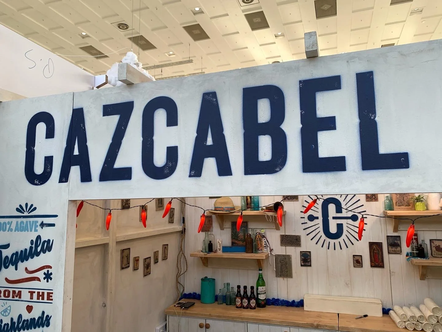 Schild mit dem Schriftzug "Gazcabel" in einer Bar mit Dekorationen wie Flaschen, Lampen, Wandbildern und Tequila-Flaschen im Hintergrund.