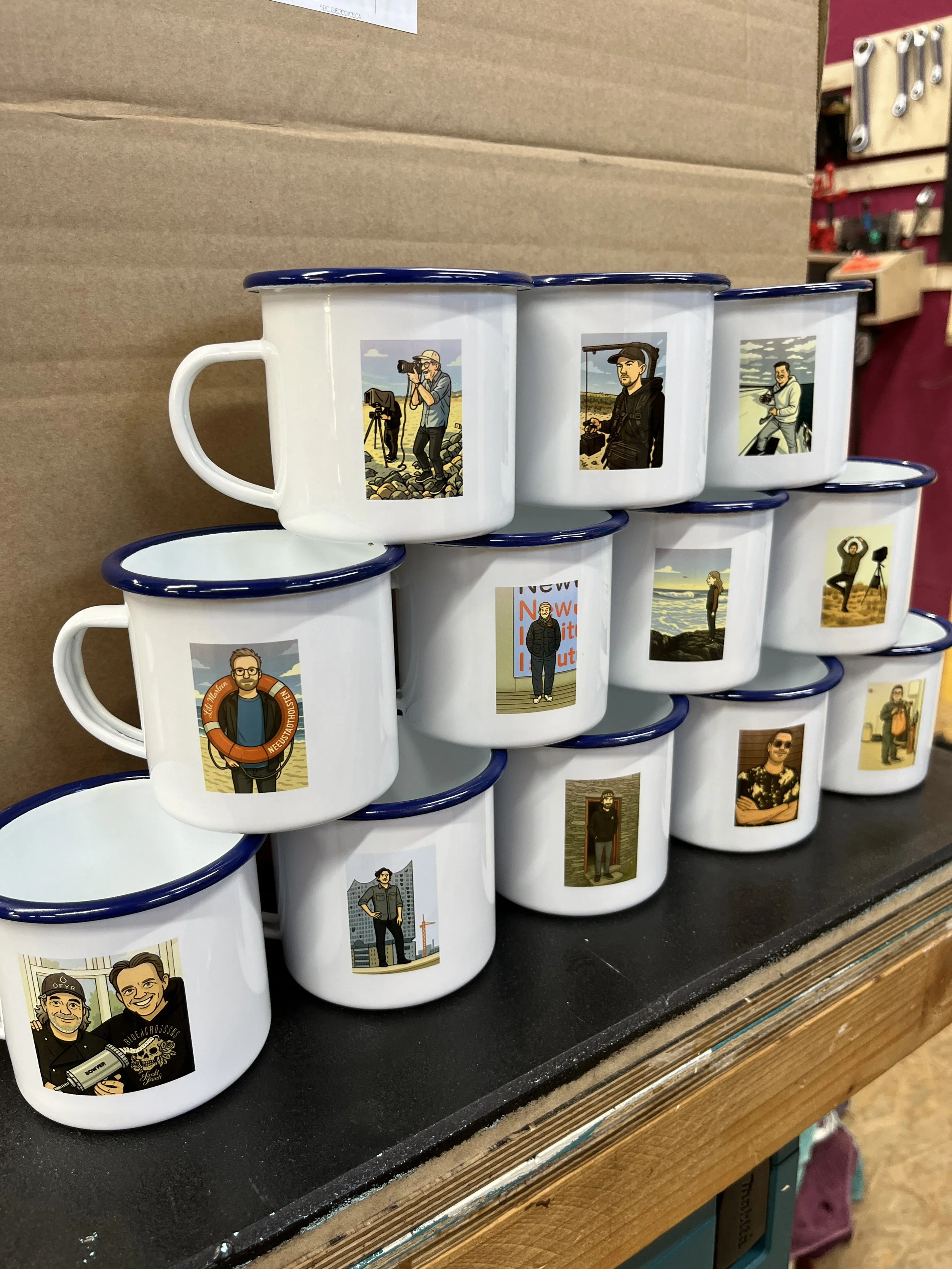Weiße Tassen mit blauen Rändern, die verschiedene Illustrationen von Männern in unterschiedlichen Szenen zeigen, stehen auf einem Holztisch.