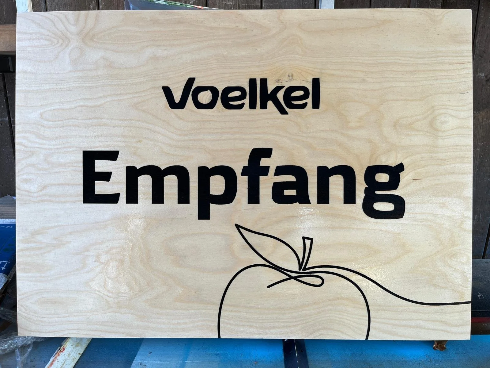 Holzschild mit der Aufschrift 'Voelkel Empfang' und einer stilisierten Apfelzeichnung.