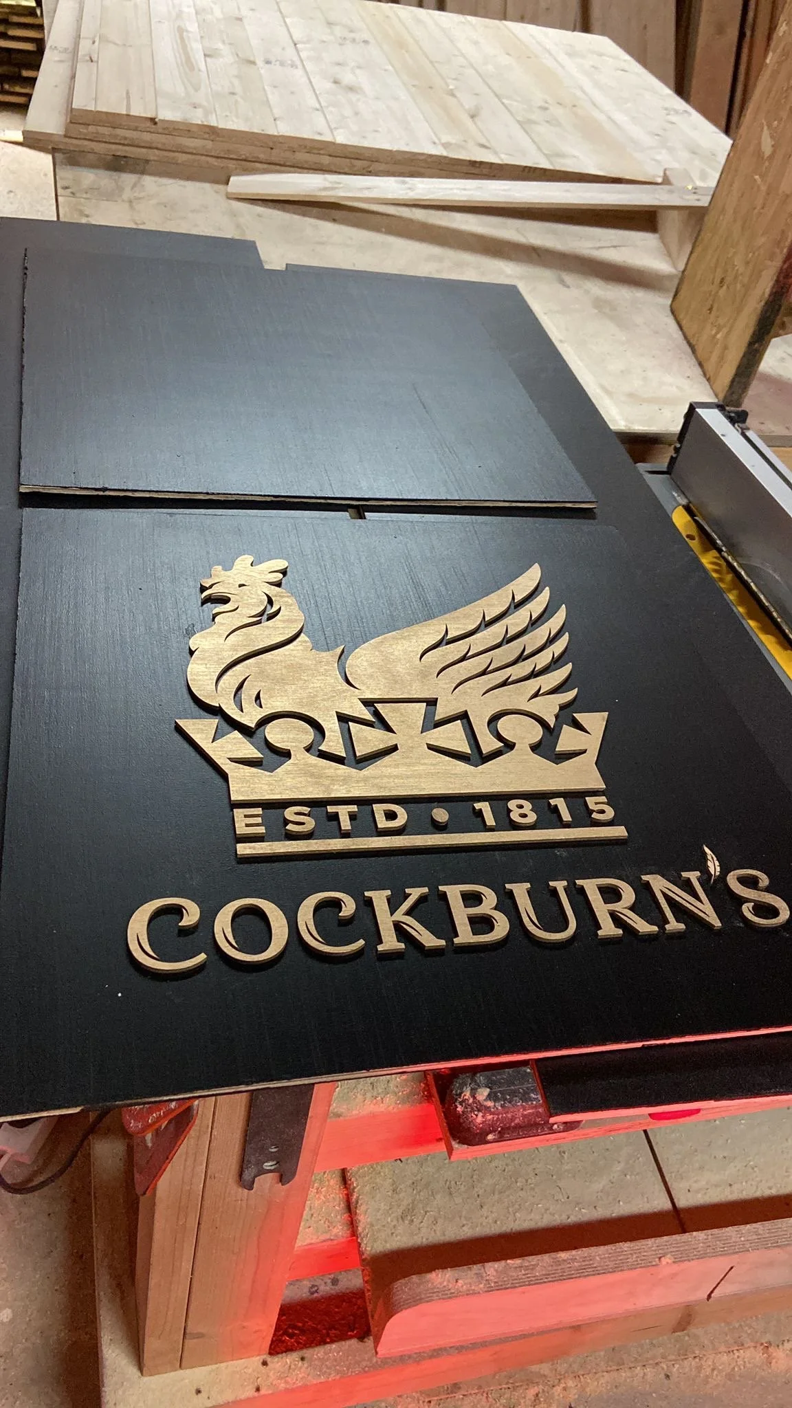Holzschnitt mit dem Logo von Cockburn's, einem Gin-Hersteller, zeigt einen griffbereiten Blick auf eine schwarze Oberfläche mit einem Holzdekor und der Aufschrift "ESTD 1815".