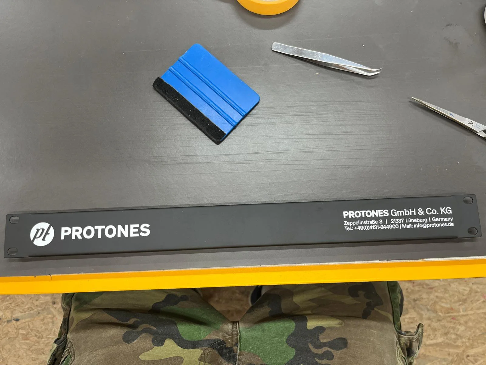 Schwarze Werkbank mit blauer Schleifbürste, einem Schneidewerkzeug, einer Zange und einem Werkzeughalter mit der Aufschrift PROTONS GmbH & Co. KG, Lüneburg, Deutschland.