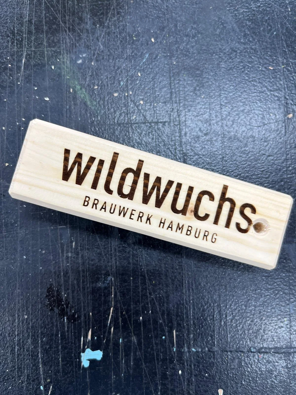 Holzschilder mit der Aufschrift "Wildwuchs Brauwerk Hamburg" auf einem dunklen Tisch.
