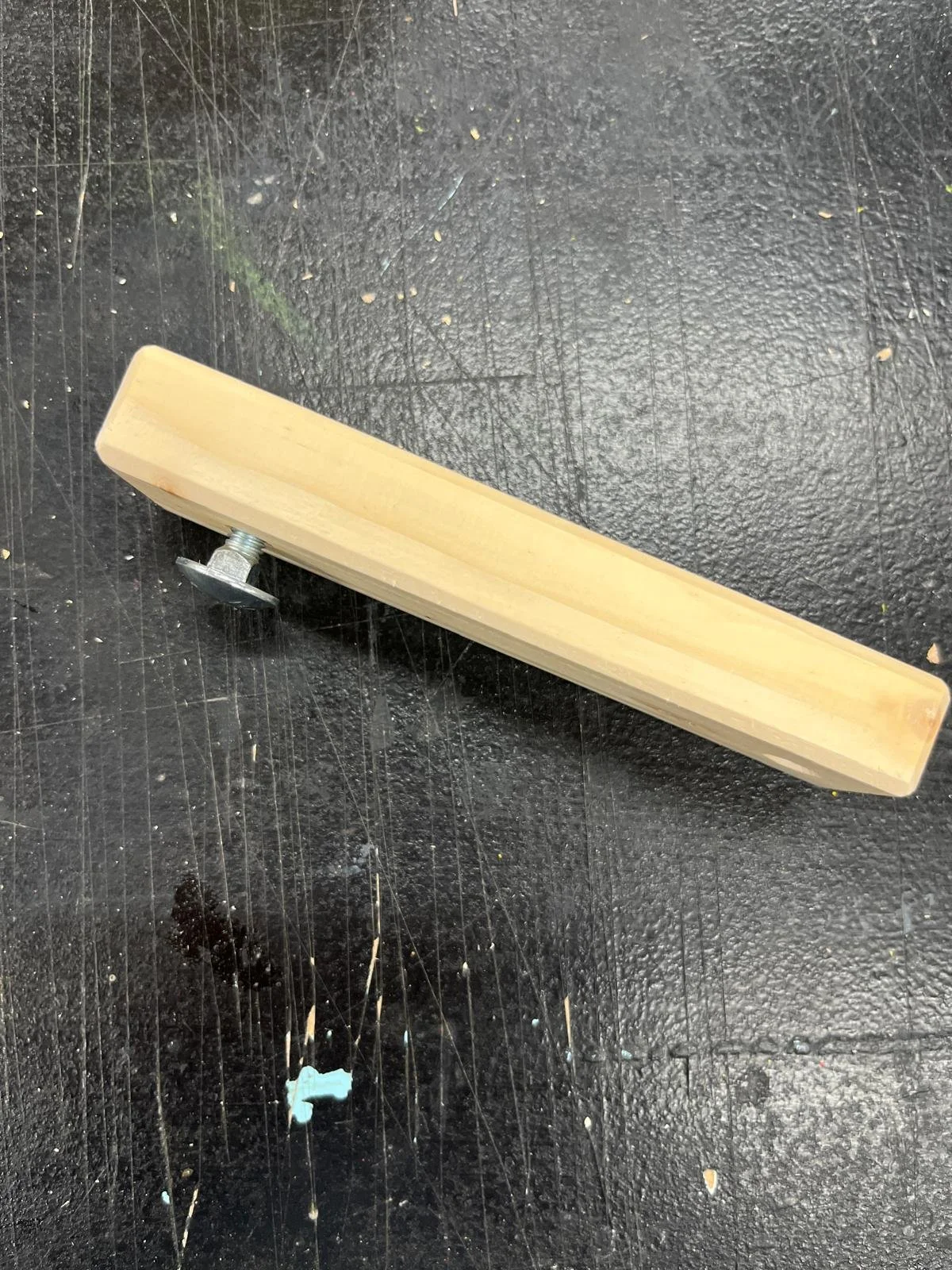 Holzstück mit Schraube auf schwarzer Oberfläche.