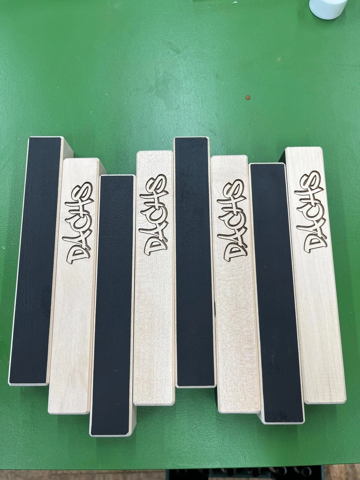 Holzplatten mit der Aufschrift ‚DACH‘, schwarz-weiße Gestaltung, auf grüner Oberfläche.