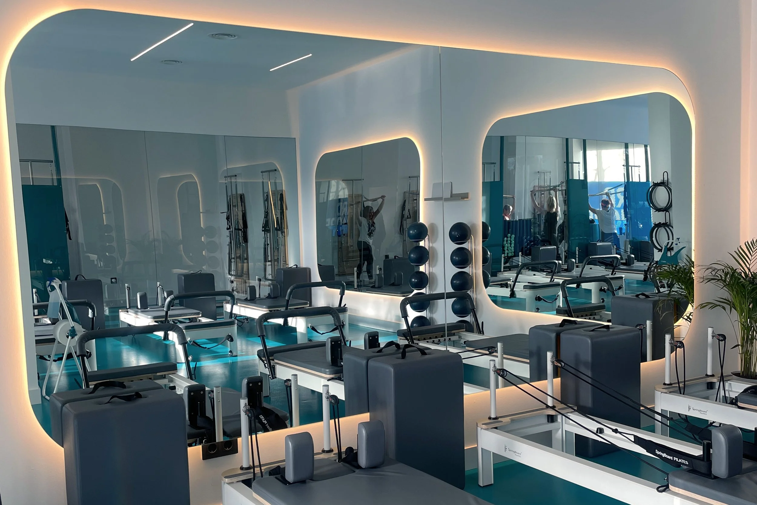 Interior de un gimnasio moderno con equipos de ejercicio, espejos y una iluminación suave en el techo.
