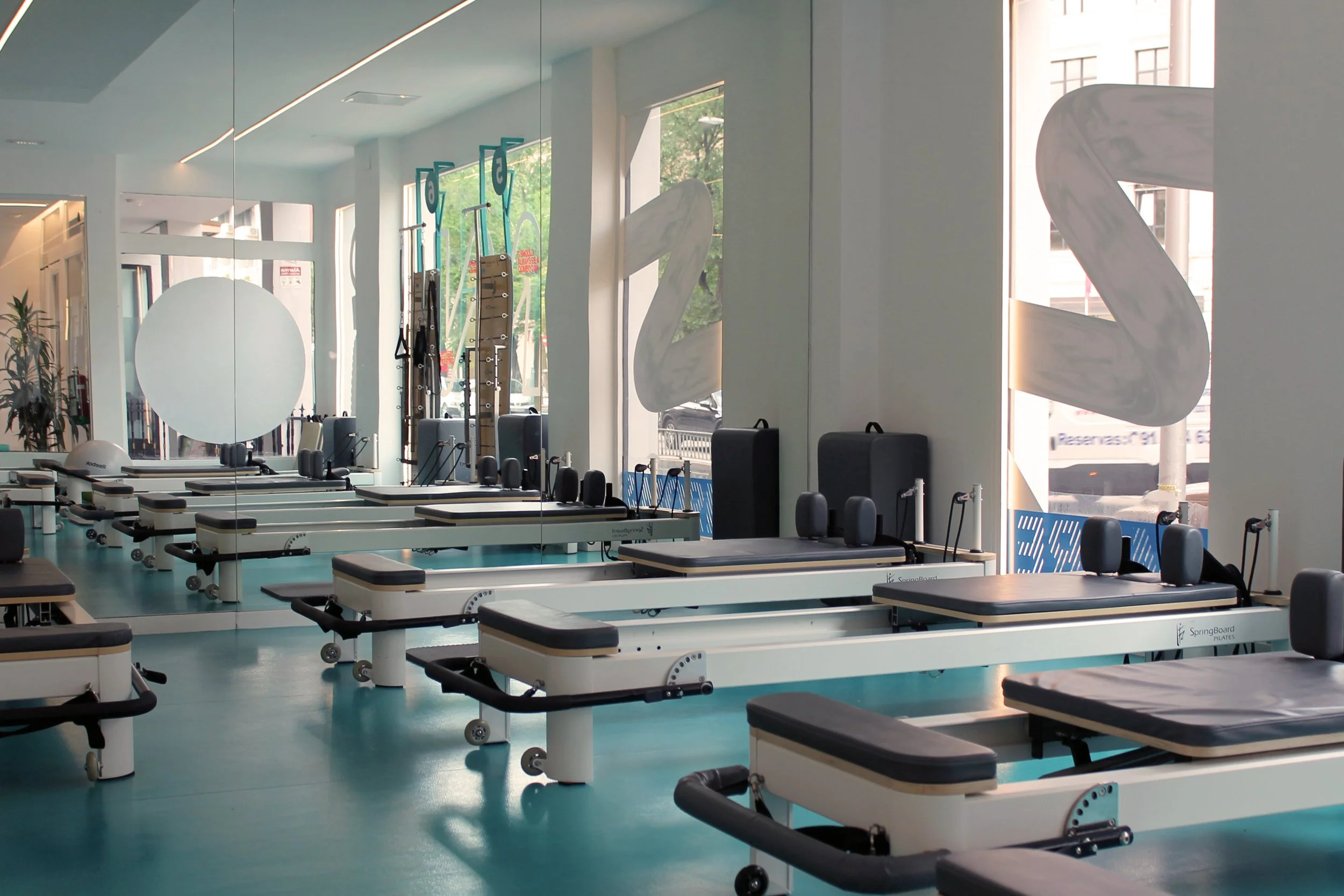 Sala de reformer con camas de Pilates, espejos grandes en la pared, y ventanas que dejan entrar luz natural.