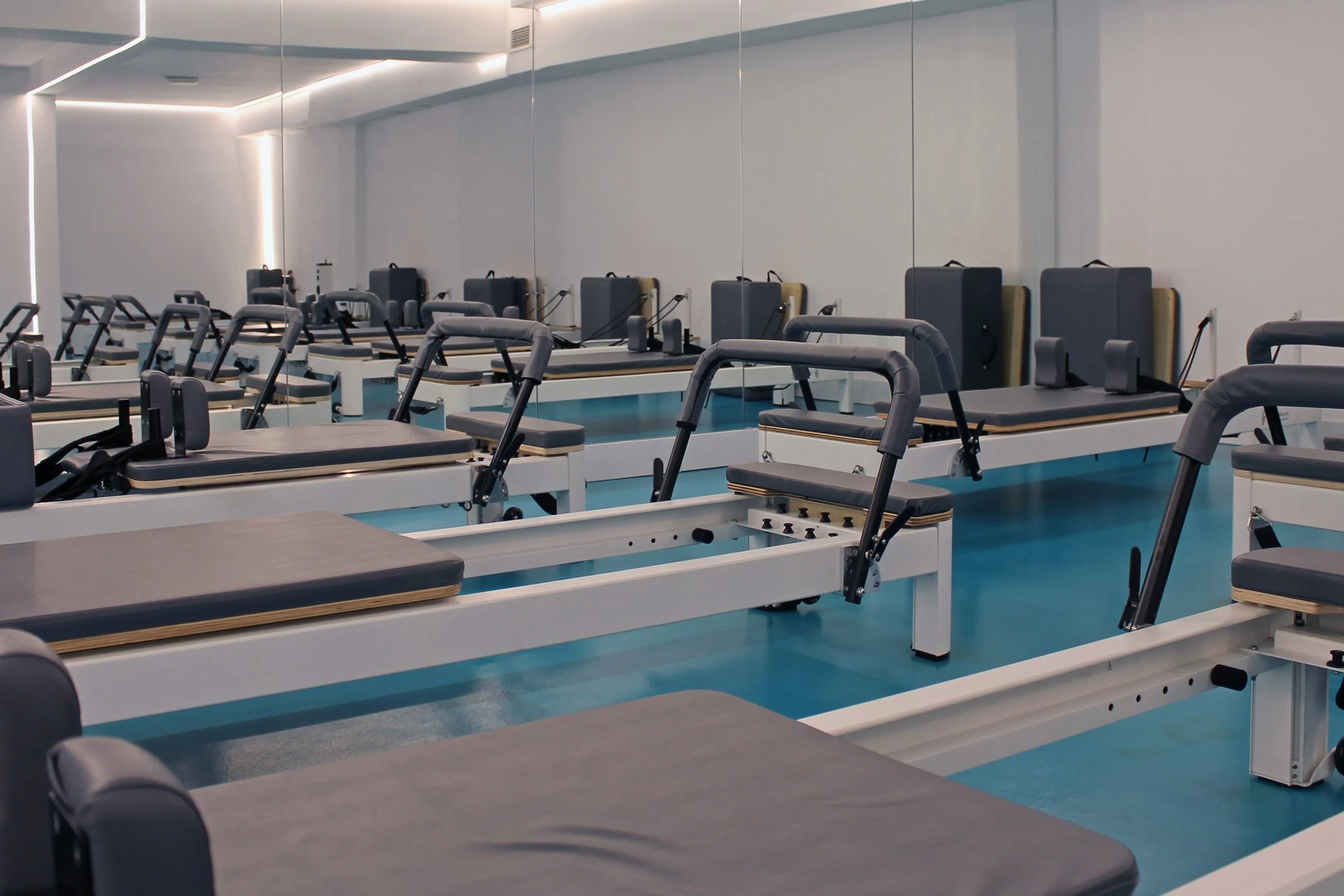 Sala de Pilates con varias máquinas y colchonetas en un espacio moderno, con paredes blancas y suelo azul.