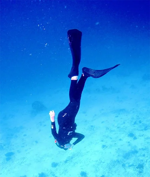 Person scuba diving underwater with fins and wetsuit, floating in the ocean