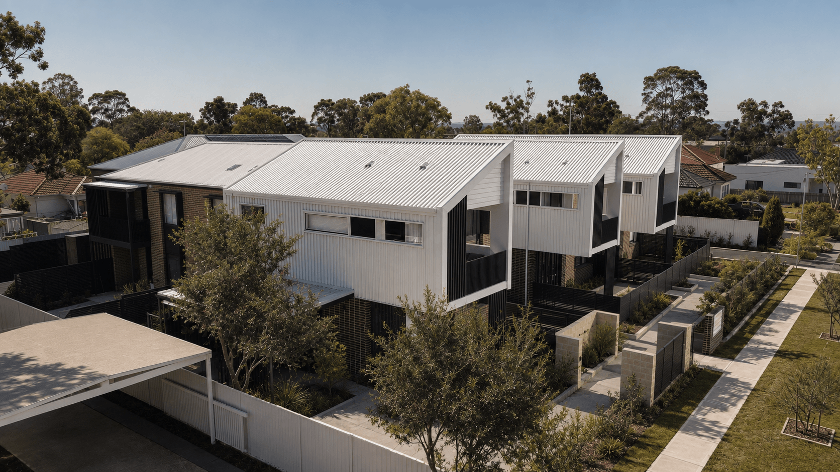 A modern multi-story residential building with white metal roofing, black and white exterior walls, and a landscaped yard with trees and pathways.