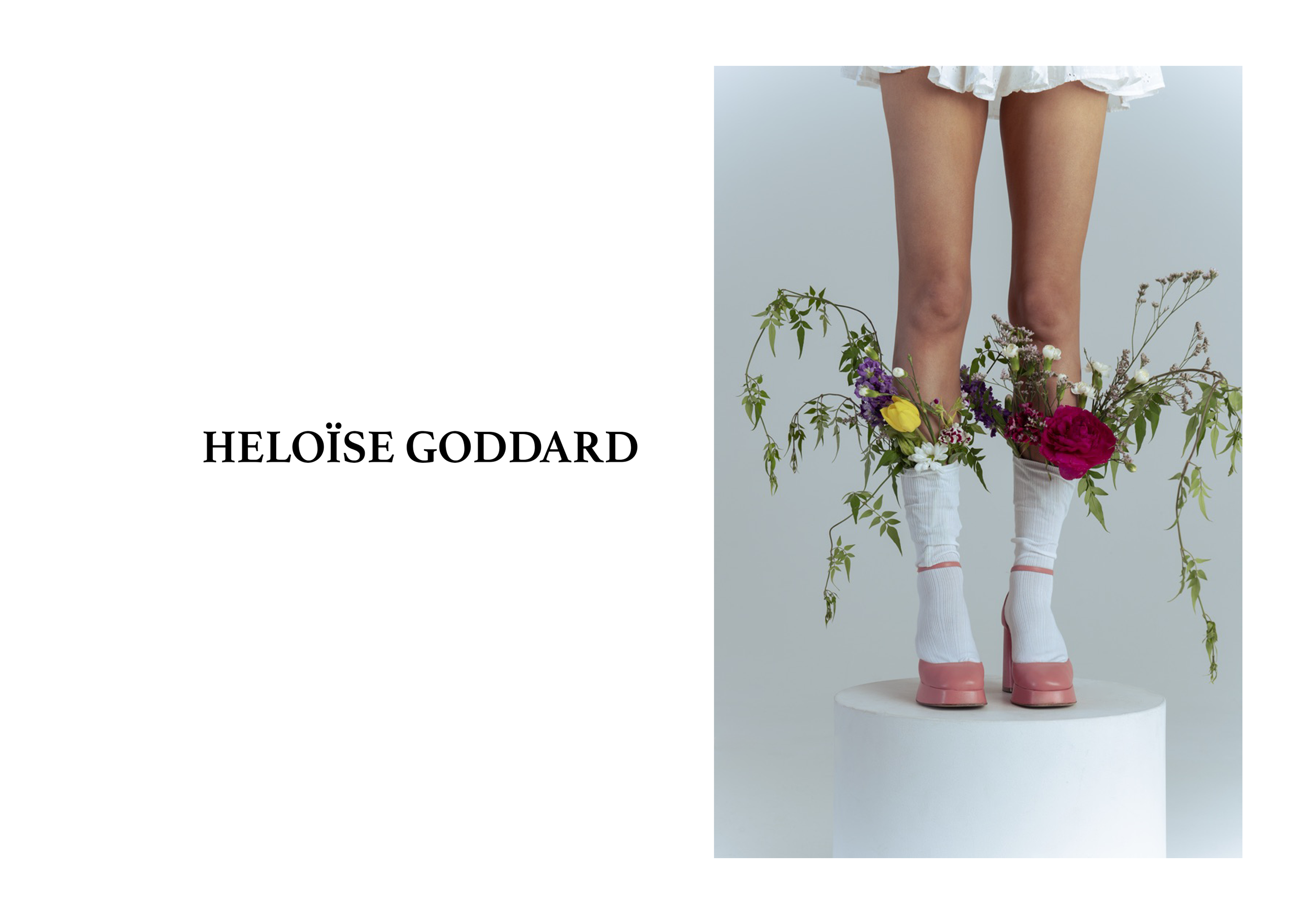 A person wearing pink rain boots and white socks, standing on a white platform with a light blue background, surrounded by colorful flowers and greenery.