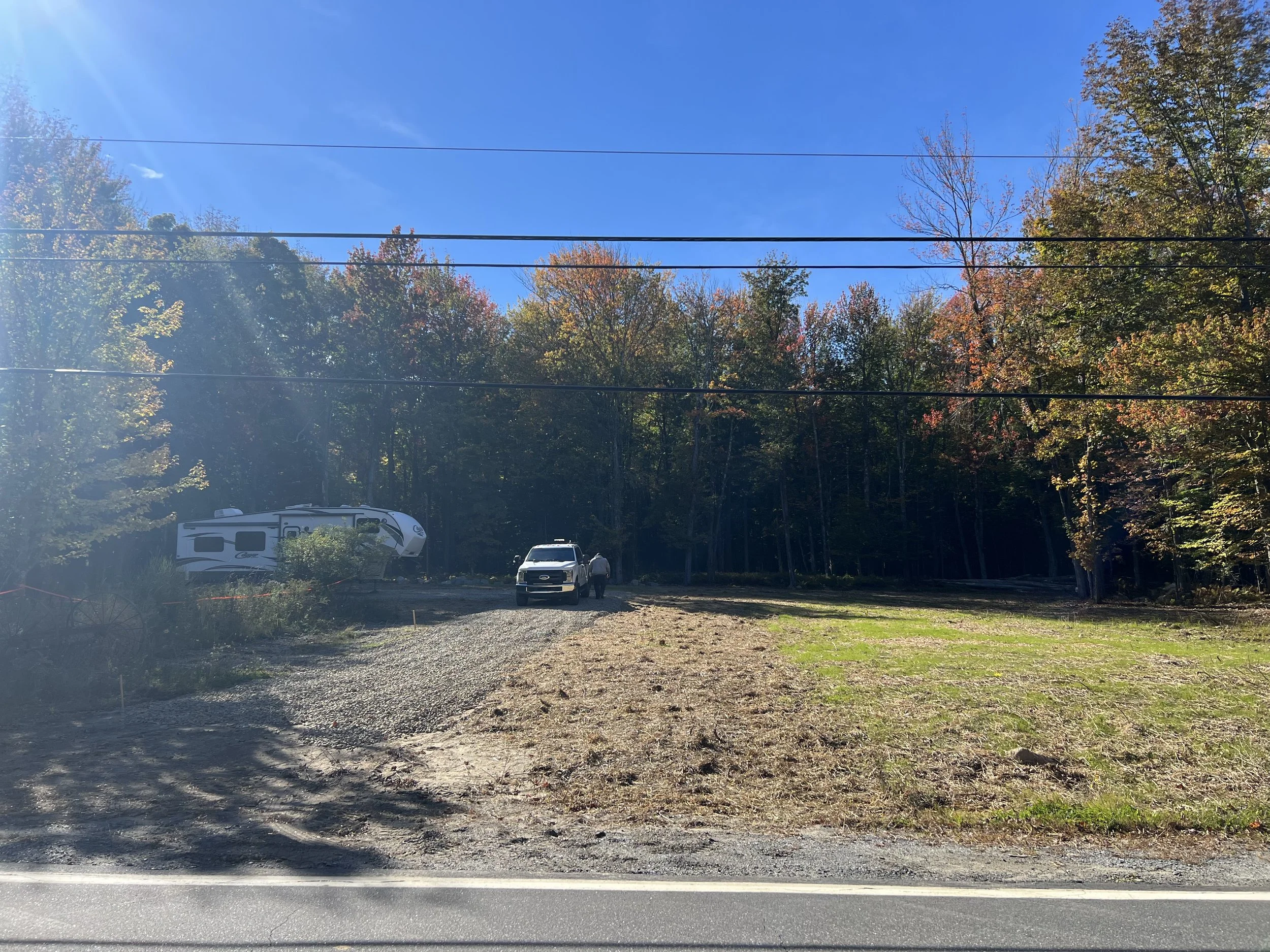 A scene of trees with fall foliage, power lines, and a parking lot with cars and a camper trailer.