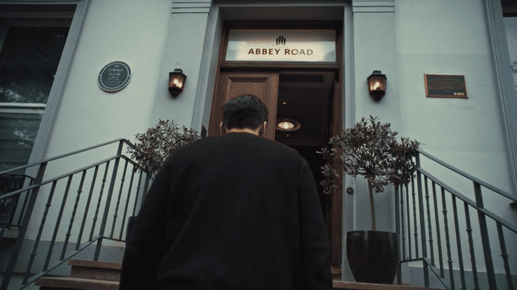 Person with dark hair and black clothing approaching the entrance of a building with a sign that reads 'Abbey Road'.