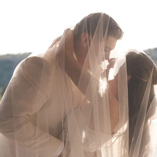 A bride and groom sharing a kiss under a sheer veil outdoors.